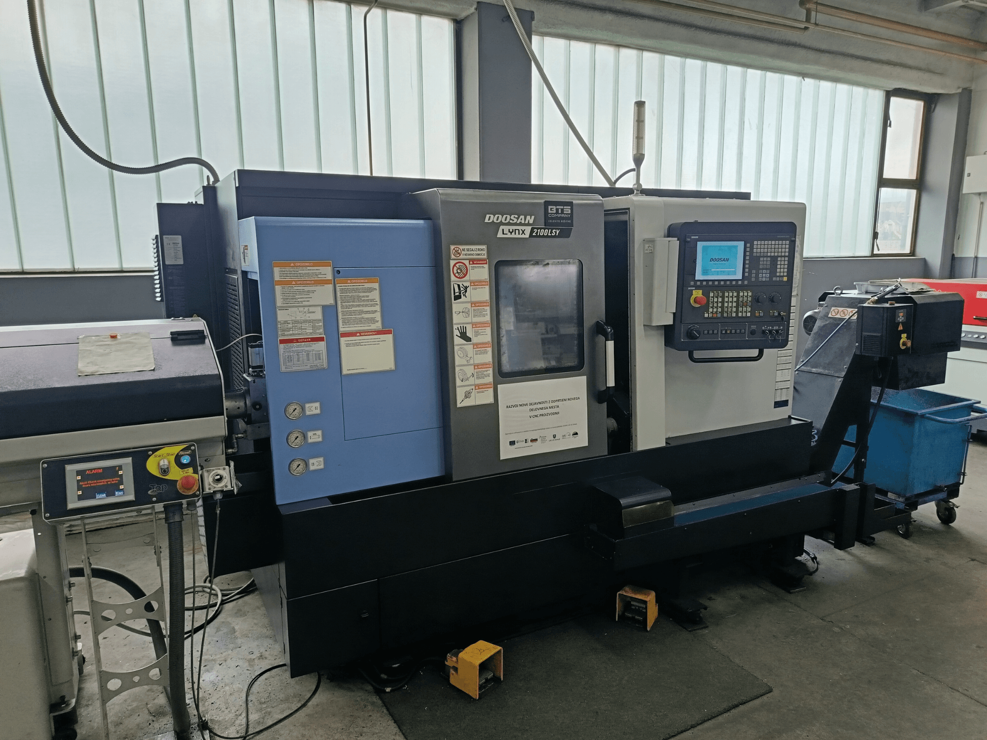 DOOSAN LYNX 2100 LSY treipingi keskuse külgvaade, kus on näha juhtpaneel ja juhtnupud, millel on nähtavad infosildid.