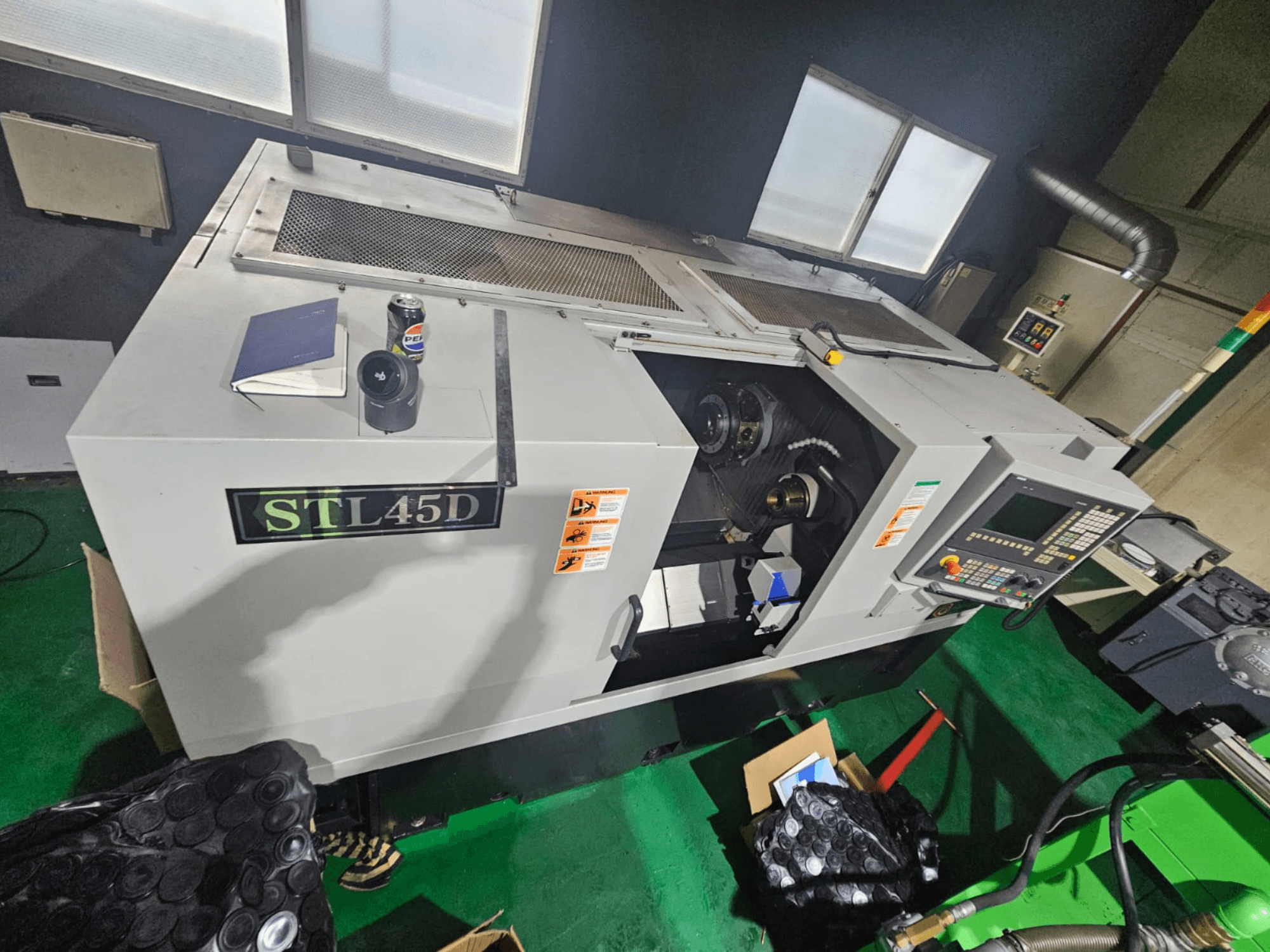 STL45D CNC-tööpink ülevalt vaadatuna, kus on näha juhtpaneel, silindriline detail, sülearvuti ja purgi peal.