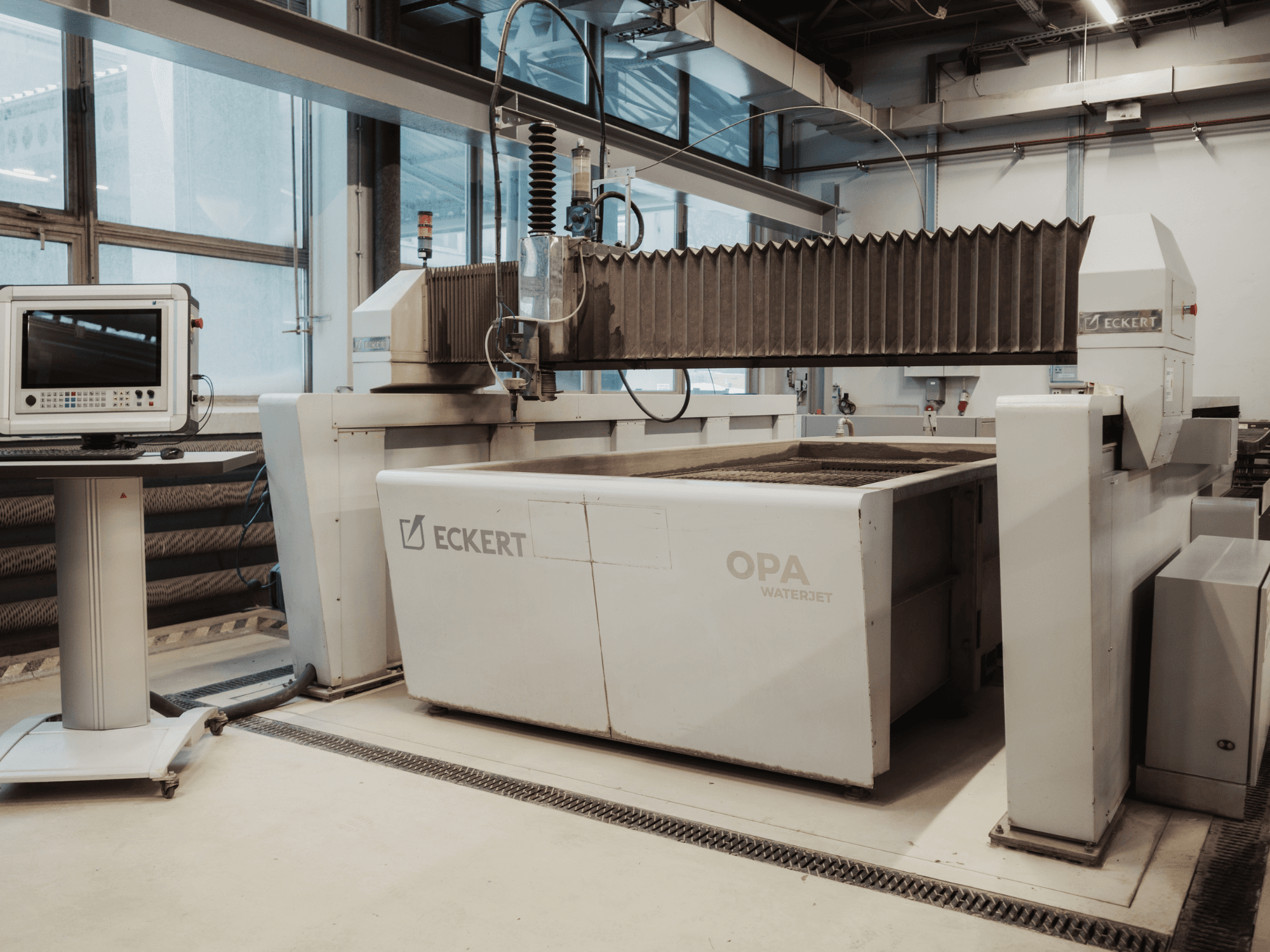 Töökojas asuv ECKERT OPAL veejet-lõikemasin, pildil vaadatuna eestpoolt, kõrval juhtpult.