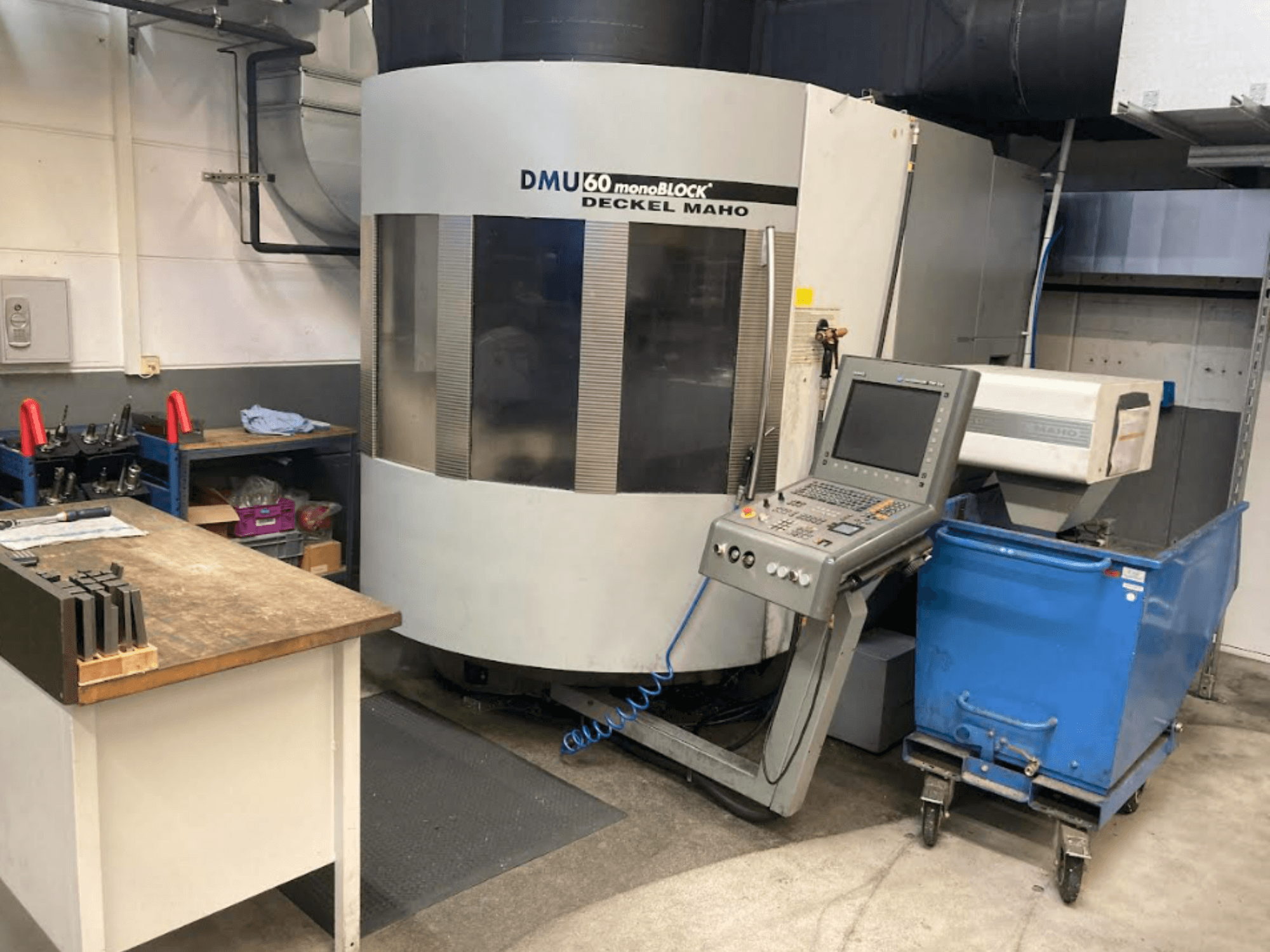 DMG MORI DMU 60 Monoblock vertikaalne töötluskeskus, esivaade, kus on näha juhtpaneel, tööruum ja sinine tööriistakäru.