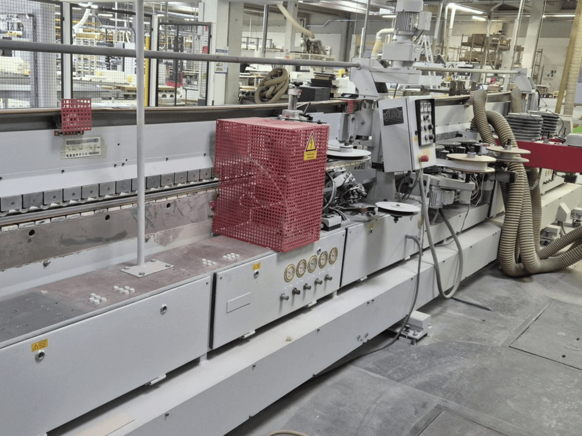 Äärelõikamismasin koos juhtpaneeli, imemisvoolikute ja punase turvakattega, külgvaates.