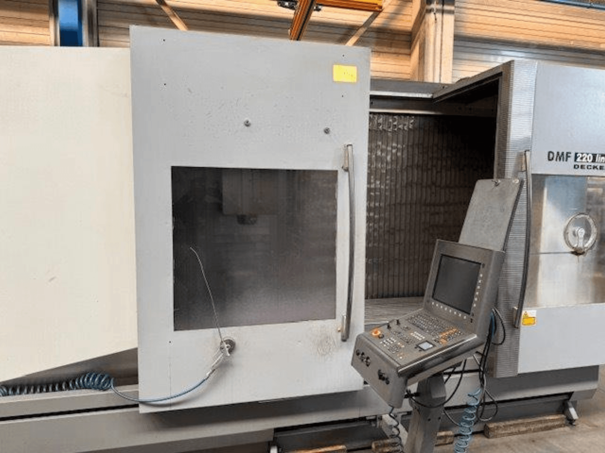DECKEL MAHO DMF 220 lineaarse vertikaalse töötlemiskeskuse esiplaan, kus on näha juhtpaneel ja avatud masina uks.