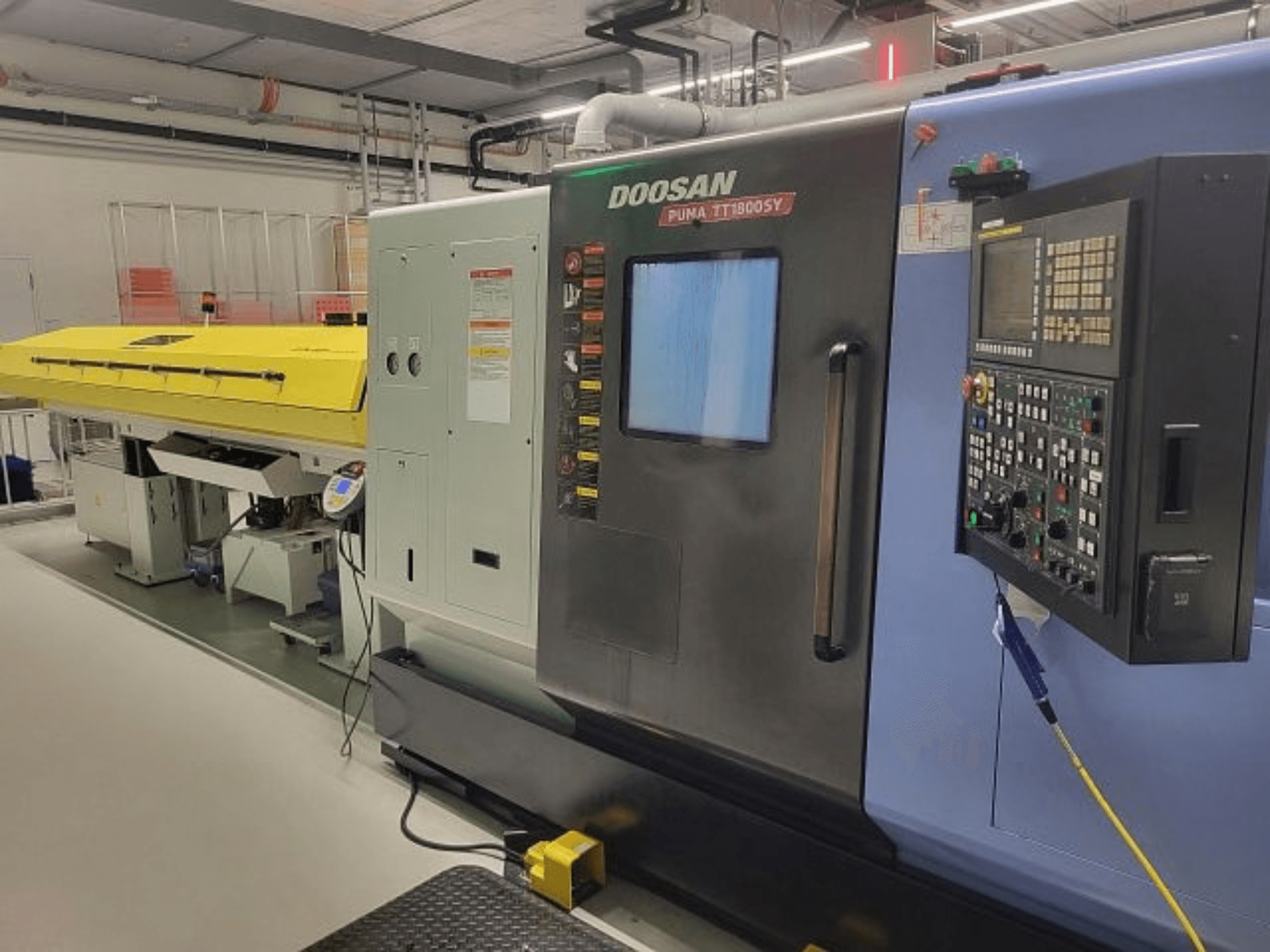 DOOSAN PUMA TT 1800 SY treimis- ja freesikeskus, vaade eest koos juhtpaneeli ja kollase kaitsekattega, tööstuslik keskkond.