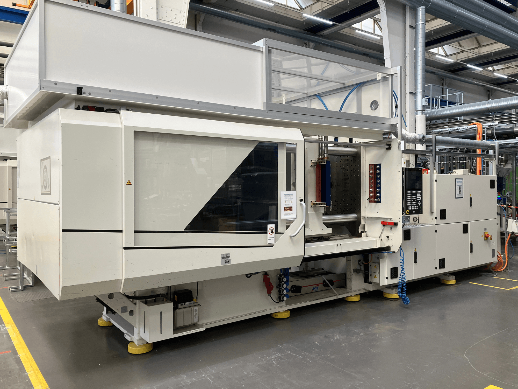 Külgvaade survevalu masinast, mudel AET, millel on juhtpaneel ja läbipaistvad katted, tööstuslikus keskkonnas.