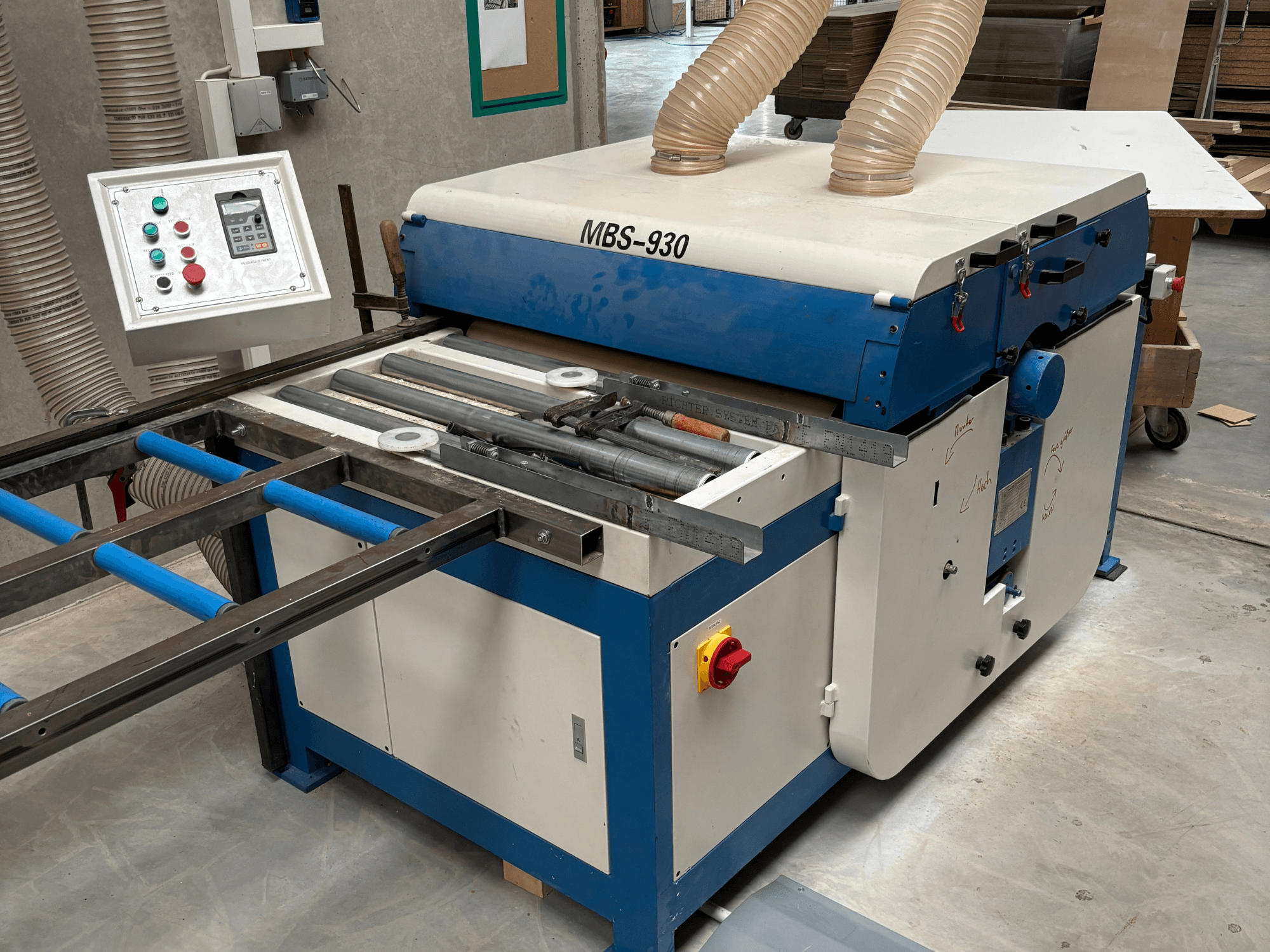 MBS-930 puidutöötlemismasin koos juhtpaneeli ja rullidega, küljelt vaadatuna, tolmueemaldusvoolikutega.