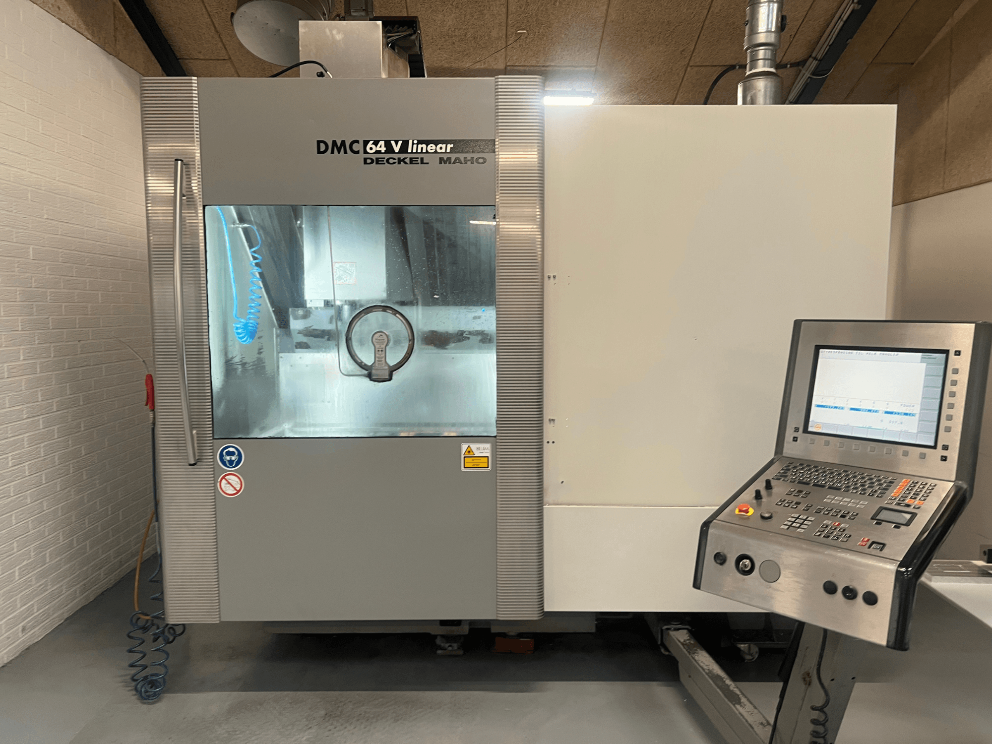 DMC 64 V Linear by Deckel Maho, CNC-töötluskeskuse esivaade, kus on näha juhtpaneel ja jahutusvedeliku düüs.