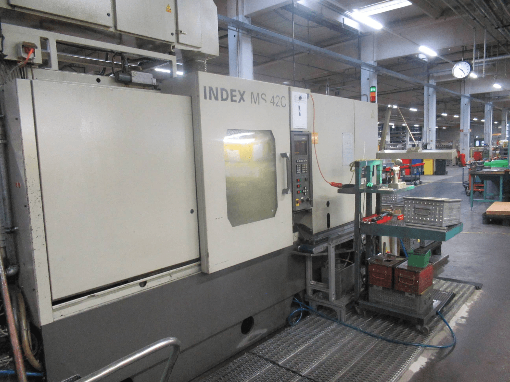 INDEX MS 42C CNC-tööpink töökojas, külgvaates on näha juhtpaneel ja tööriistade hoiustamine ratastel kärus.