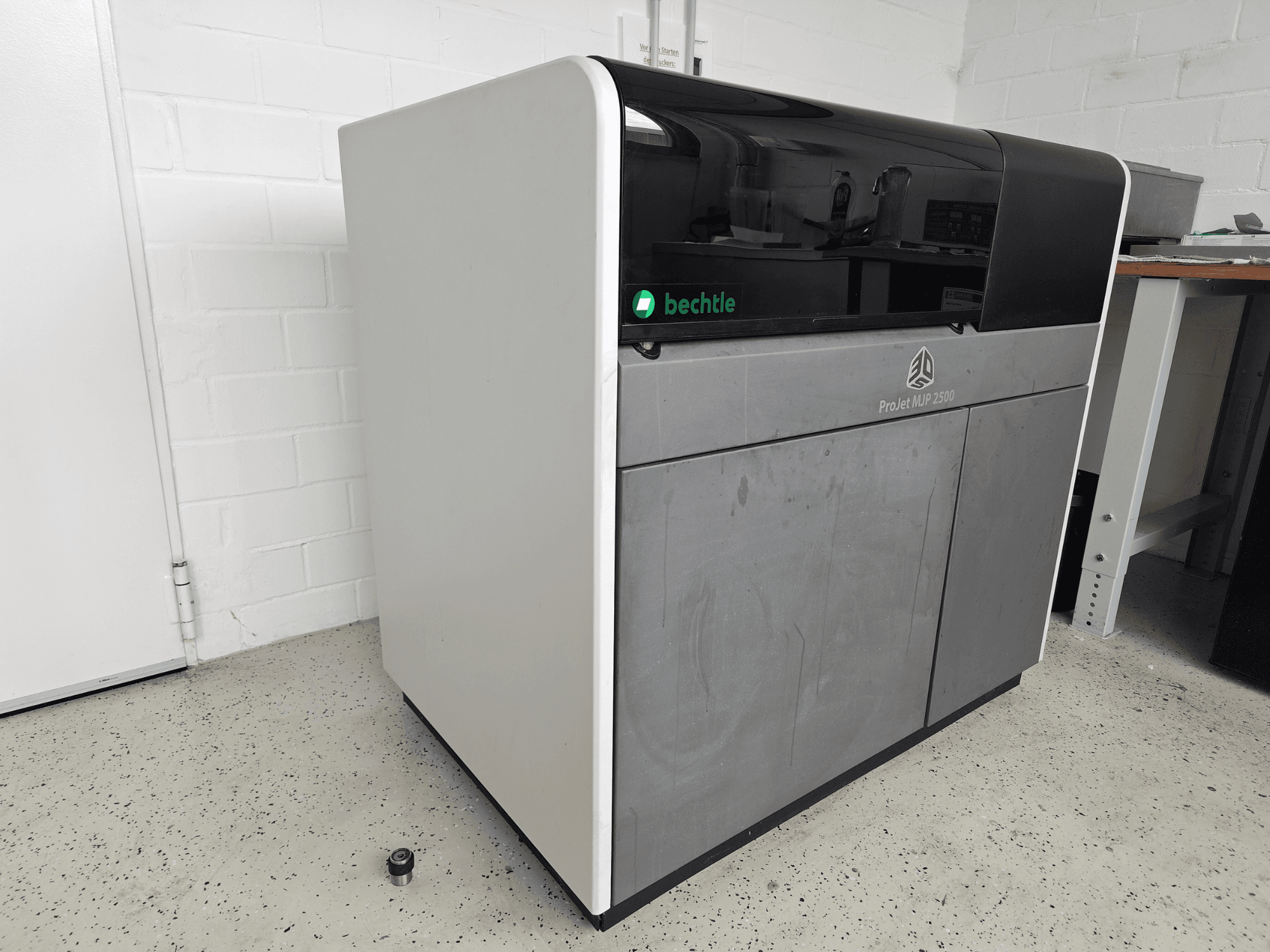 3D Systems ProJet MJP 2500 Plus plastprinteri vaade eest; seadmel on elegantne disain, millel on tume ülaosa ja heledat värvi korpus.