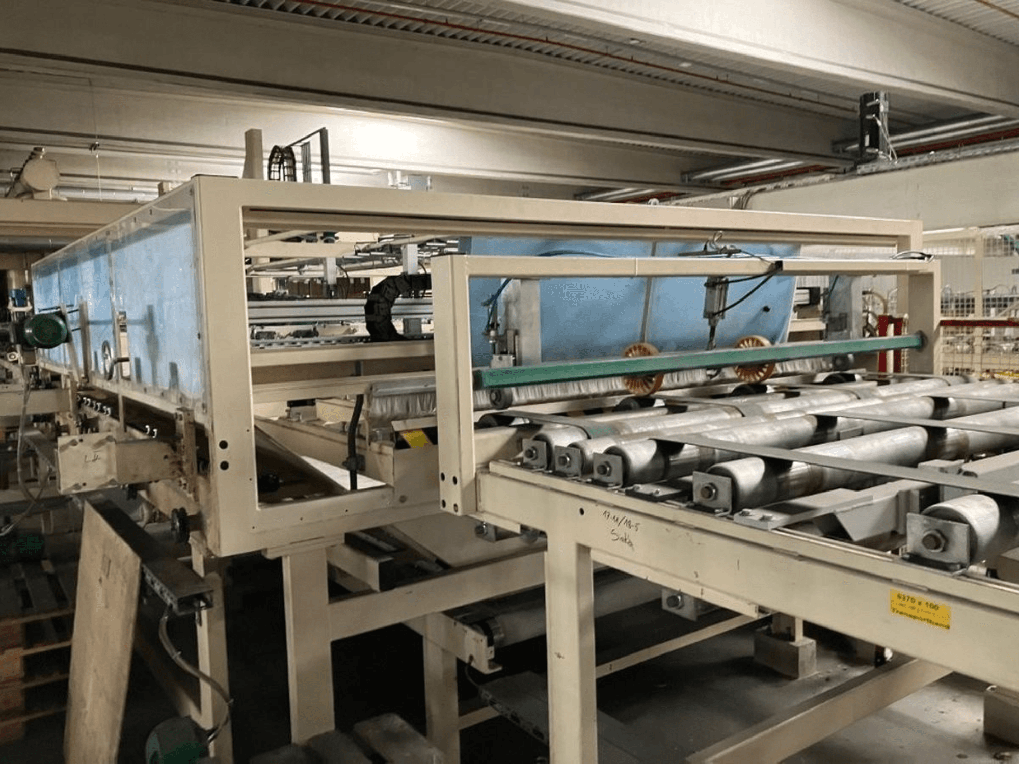 WEMHÖNER KT-F-1E lamineerimispress, külgvaade, millel on rullid ja juhtimisseadmed materjali töötlemiseks tehases.