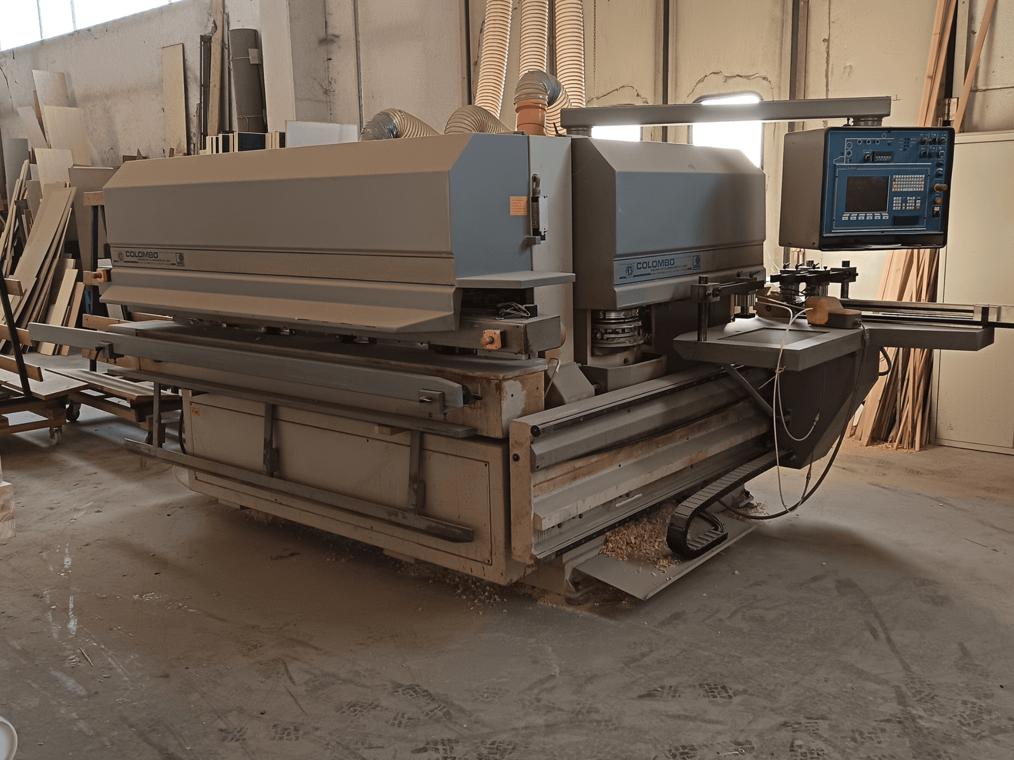 Colombo puidutöötlemismasin, külgvaade, kus on näidatud juhtpaneel, lõiketerad ja saetolmu kogunemine töökojas.