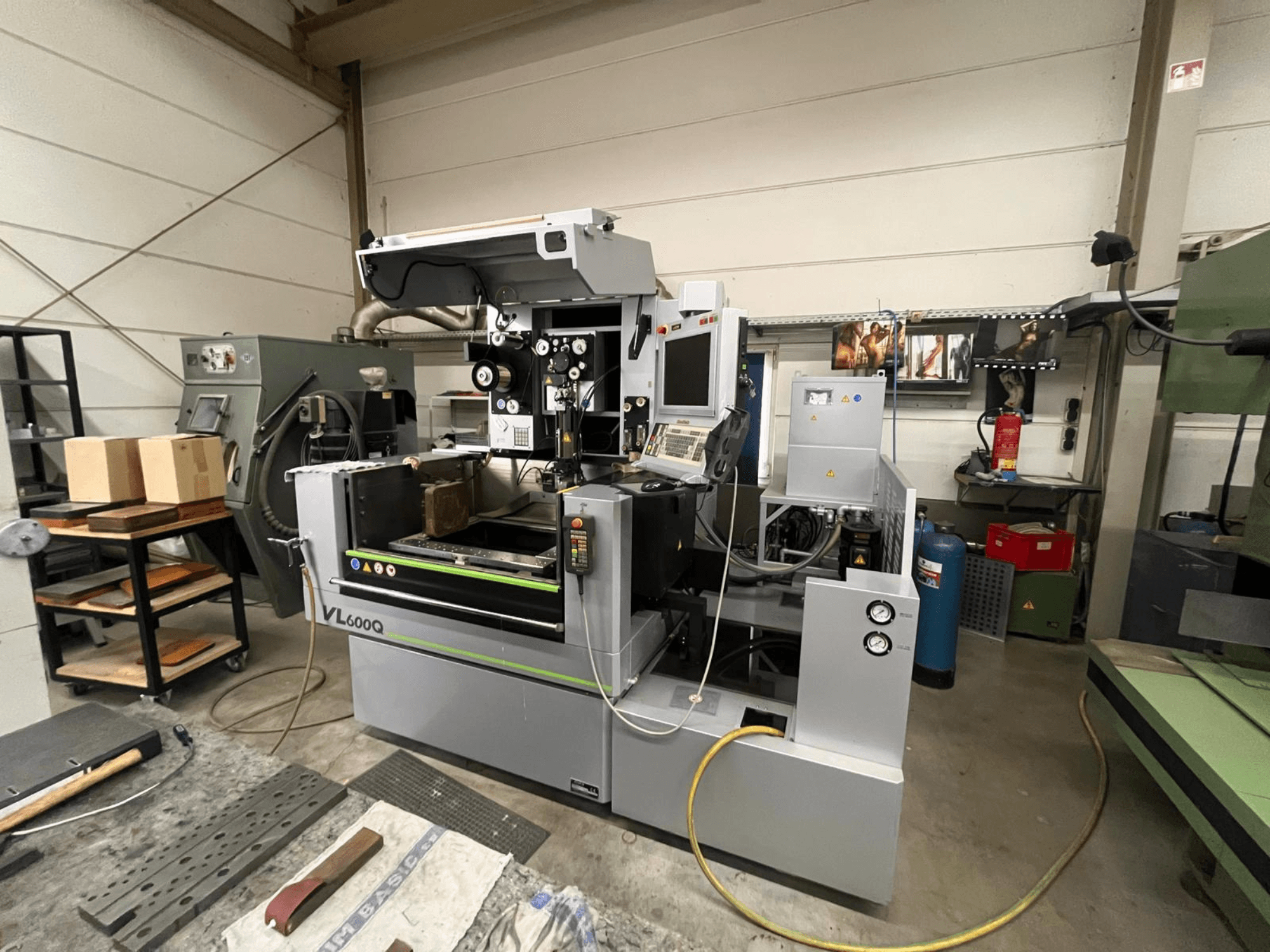 VL600Q CNC-tööpink töökojas, esivaade, juhtpaneel, materjal paigas ja erinevad tööriistad lähedal.