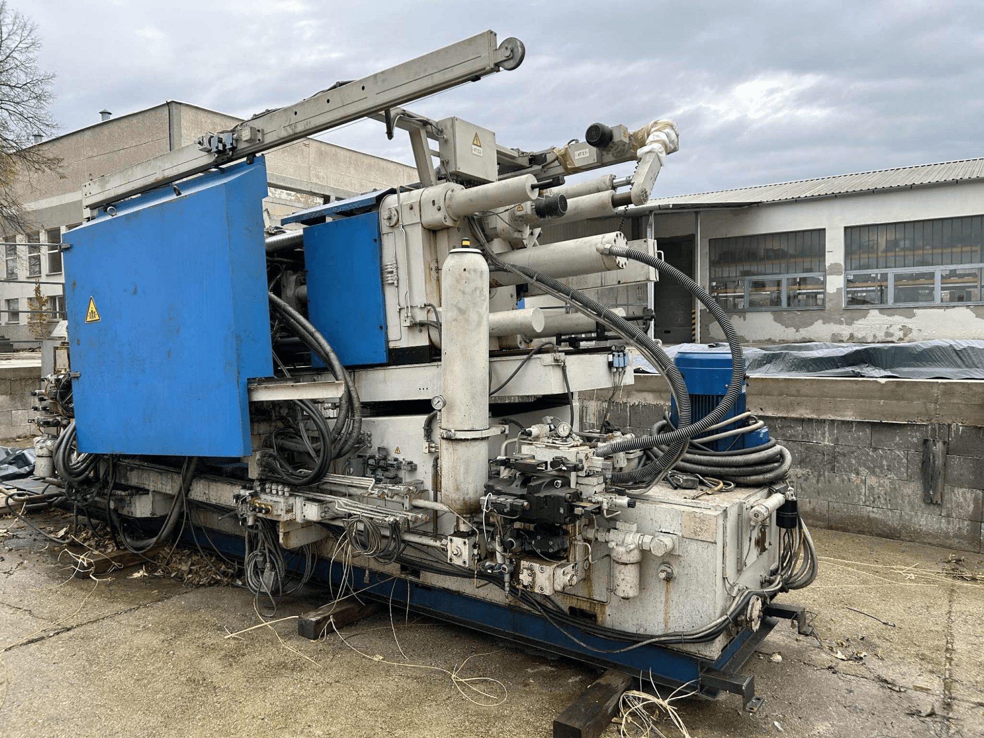 Suur tööstuslik hüdraulikamasin sinise korpuse, erinevate voolikute ja metallosadega, küljelt vaadatuna.