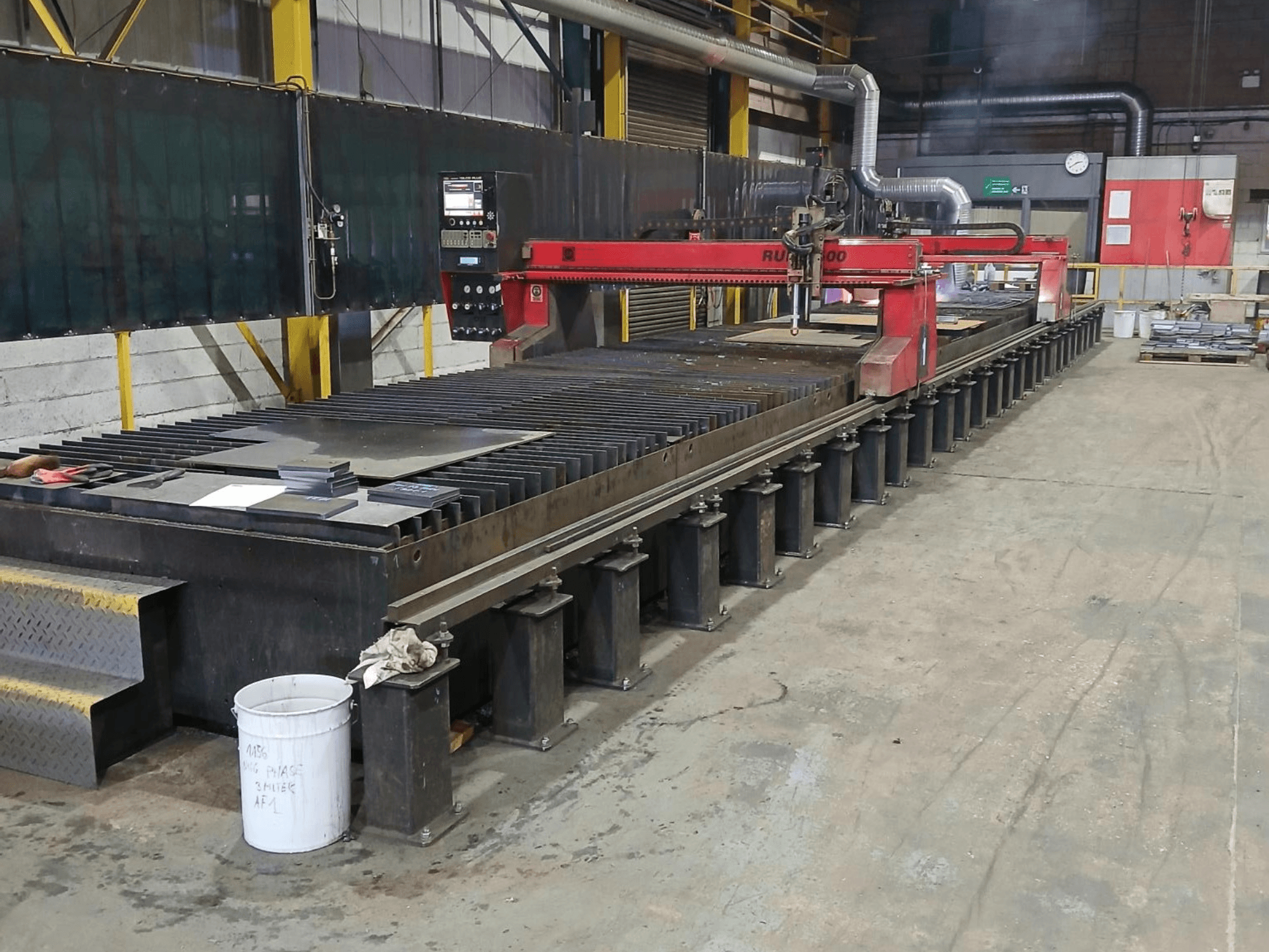 Punane RUIDA 300 lõikemasin, külgvaade, metallplaadiga teraslaual, mis asub tööstuslikus tööruumis.