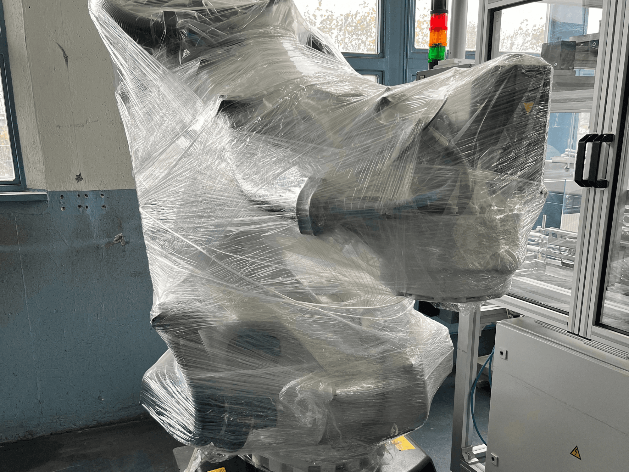 Plastiga ümbritsetud tööstusroboti käsi, esiplaanil. Sisaldab juhtseadet ja märgutuled. Marki ei ole näha.