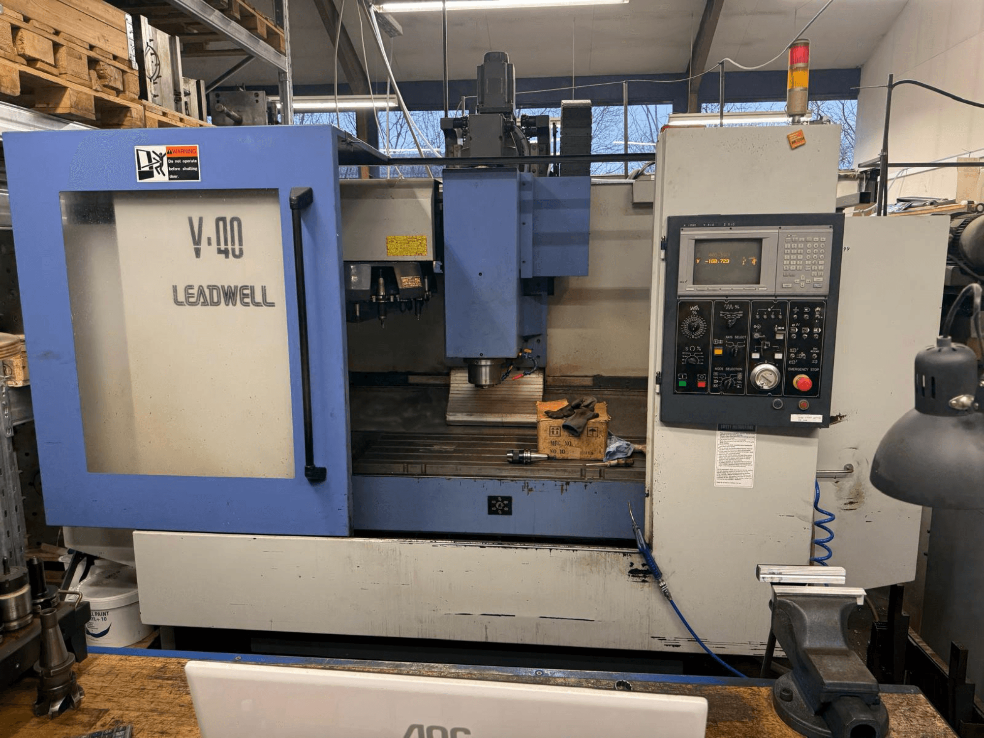 LEADWELL V-40 CNC-freespingi esivaade, millel on juhtpaneel, lõiketööriistad ja käärid tööpinkidel.