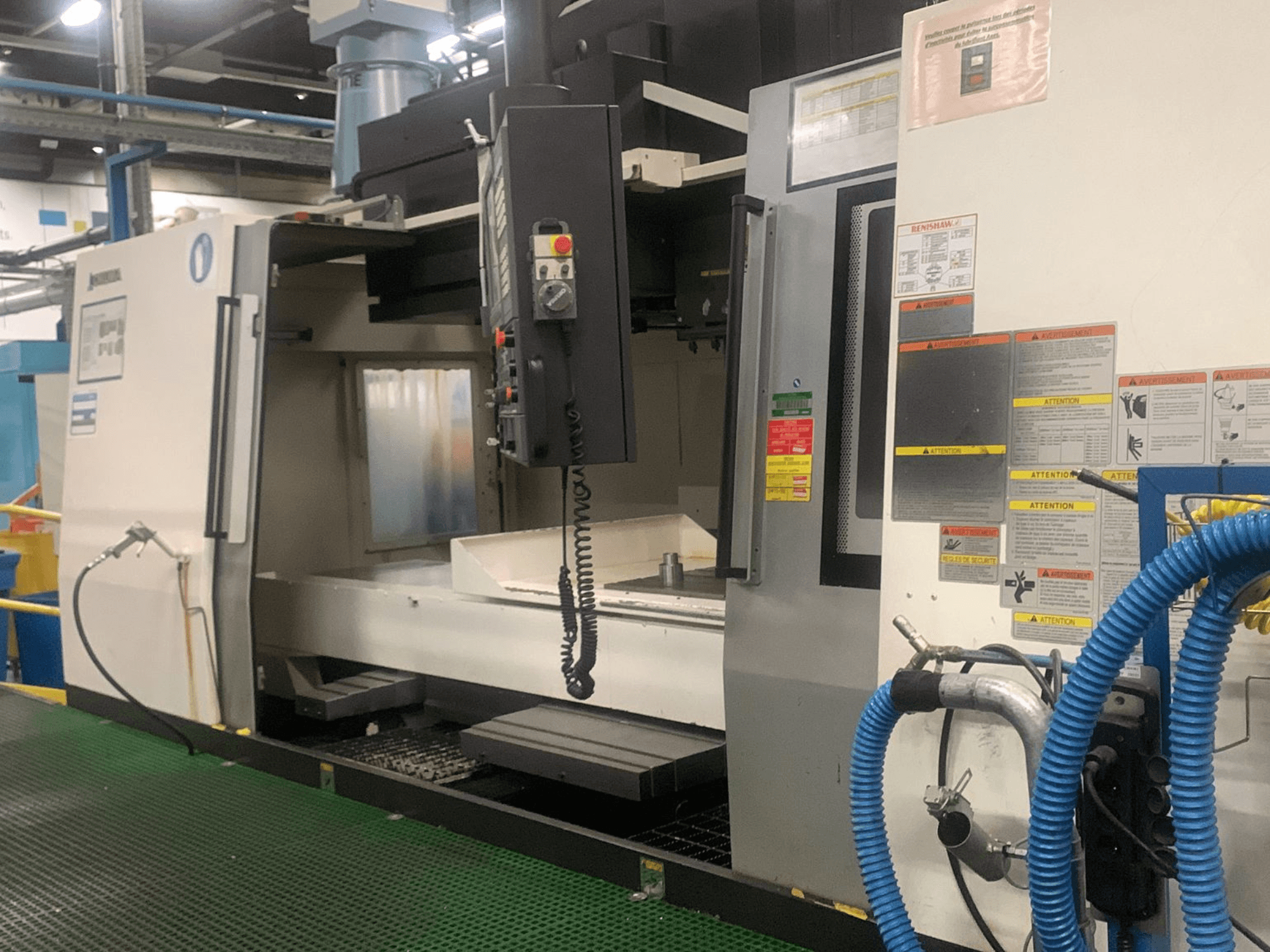 Okuma Millac 852 VII vertikaalne töötlemiskeskus, vaade eest, millel on näha juhtpaneel, spindli piirkond ja ohutusmärgised.