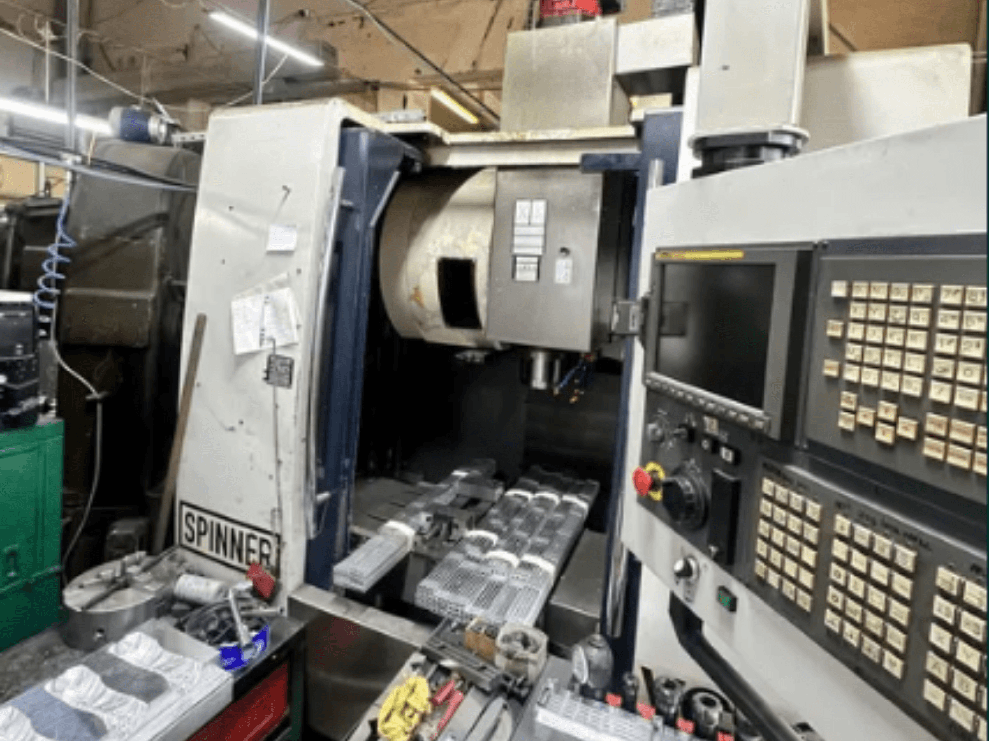 Spinneri CNC-tööpink, esiplaanil; puutetundlik kasutajaliides, tööriistad tööpinnal ja töötlemiseks valmis töödeldud detailid.
