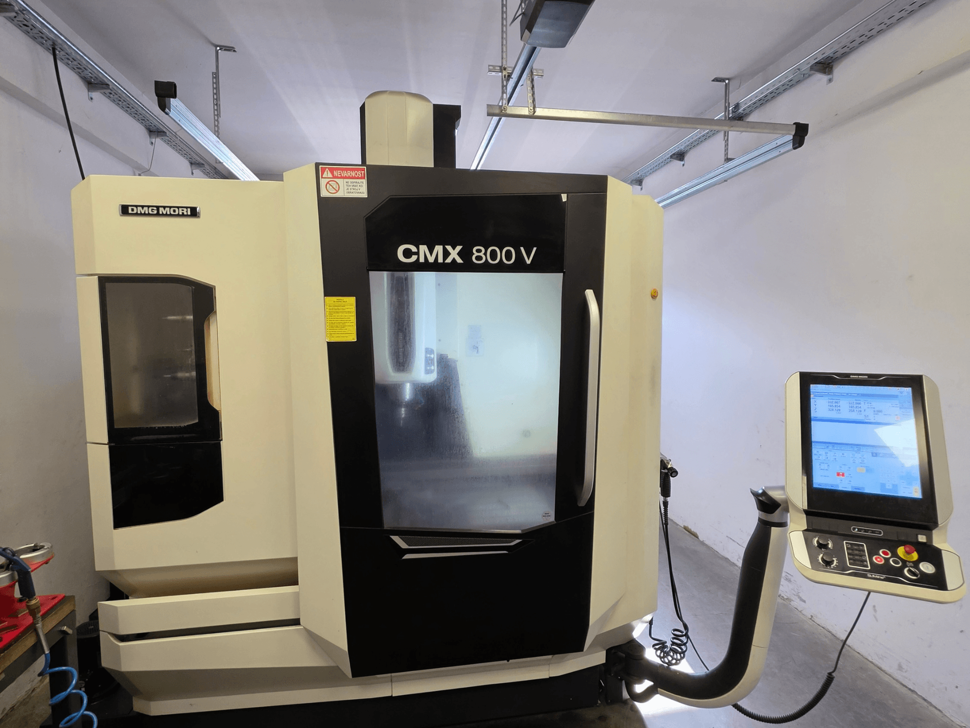 DMG MORI CMX 800V vertikaalne töötlemiskeskus, vaade eest, millel on puutetundlik juhtpaneel ja selged ohutusmärgid.
