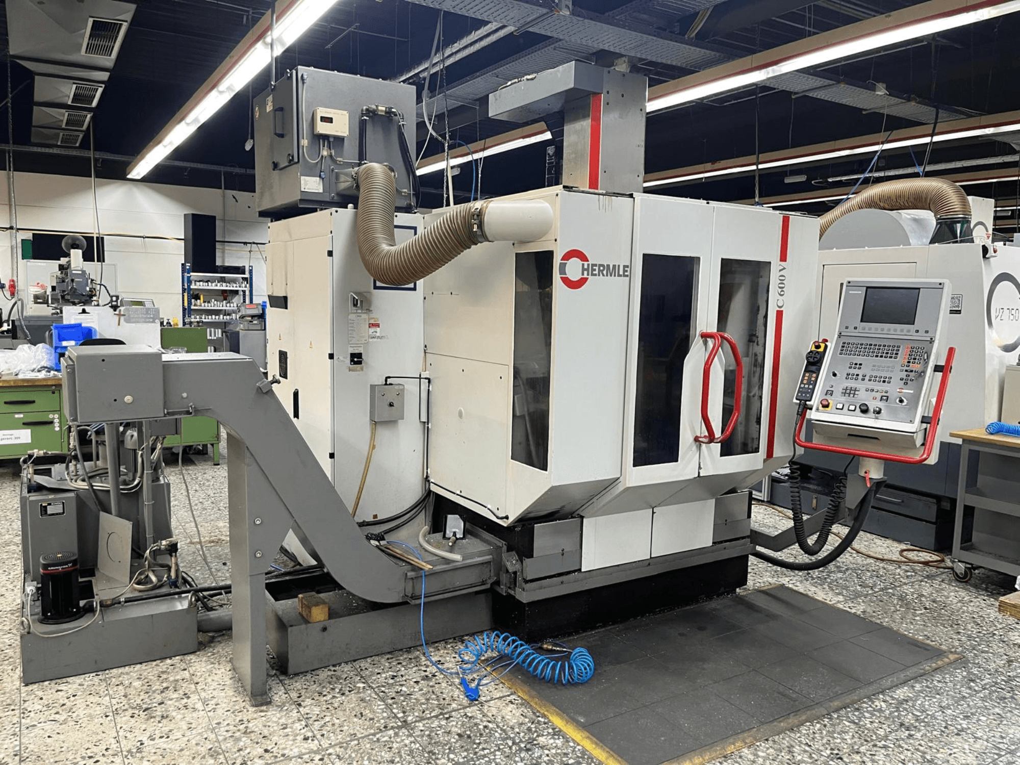 HERMLE C 600 V vertikaalne töötluskeskus töökojas, esiplaanil juhtpaneel ja ventilatsiooniseadmed.