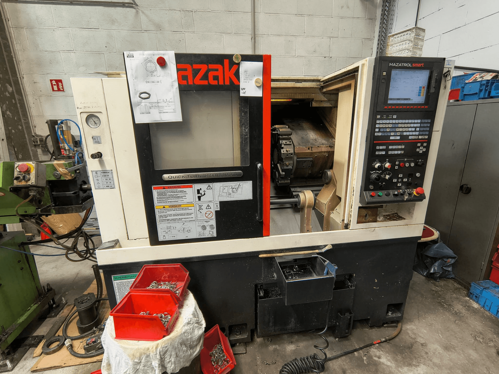 Mazak Quick Turn Smart 100 S, külgvaade, millel on näha juhtpaneel, jahutusvedeliku koguja ja kruvide hoiukastid.