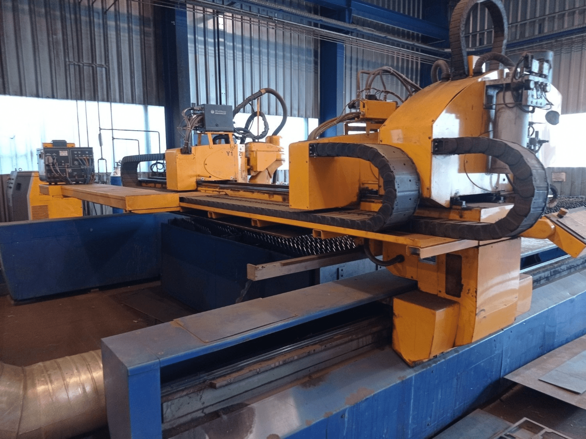 Kollane CNC-plasmalõikepink kahe horisontaalse käega, näidatud eestpoolt, koos juhtpaneeli ja lõikeplaadiga.