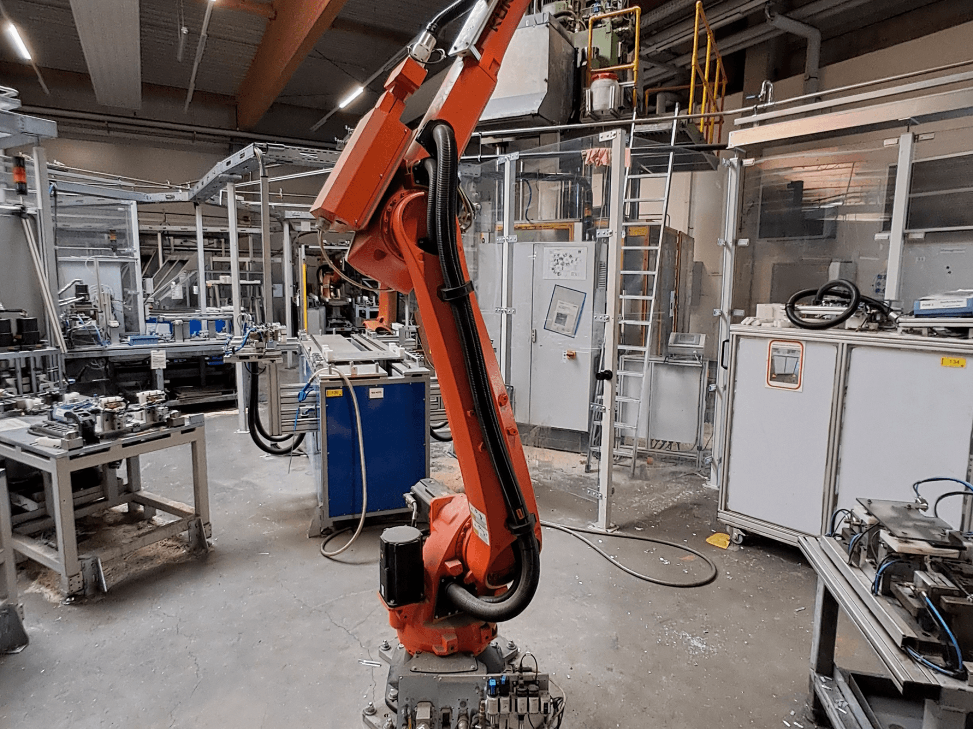 KUKA KR 26 R3100/SEL robotkäsi tööstuslikus keskkonnas, kujutatud külgvaates, taustal töötavad seadmed.