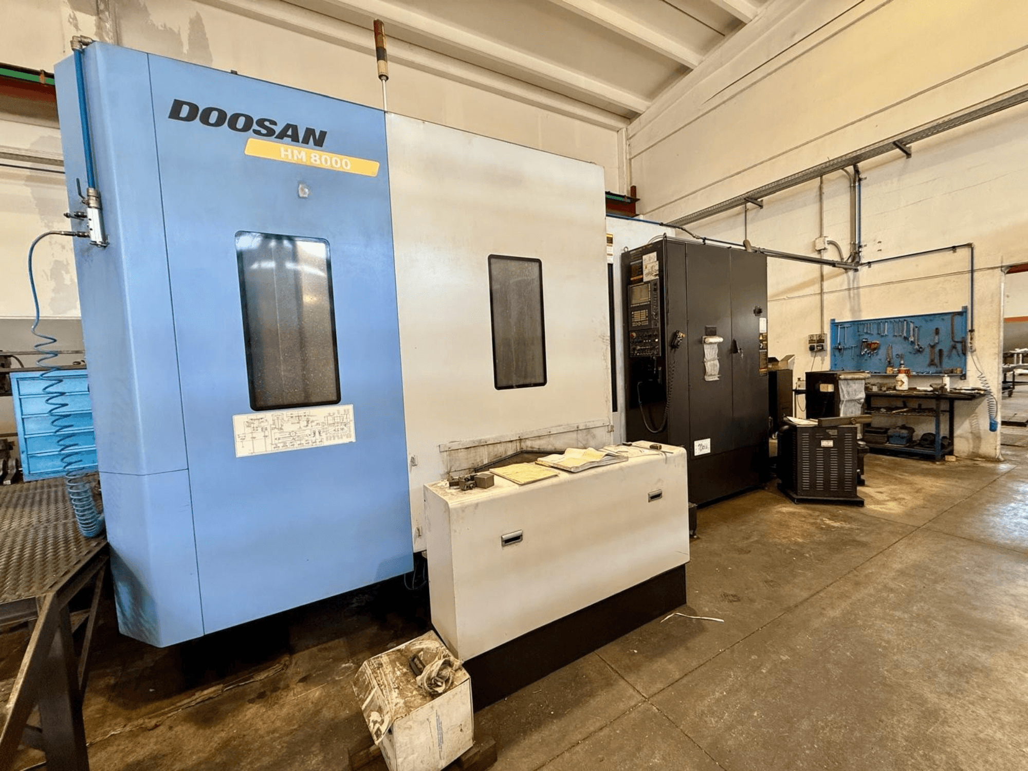 Sinine horisontaalne töötlemiskeskus DOOSAN HM 8000, vaade eest, millel on näha juhtpaneel ja selle lähedal asuvad töökoda seadmed.