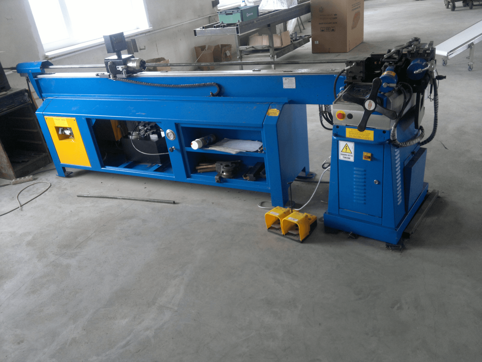 Kollaste aktsentidega sinine puidutöötlemismasin, külgvaade; juhtpaneel, jalgpedaalid ja pöörlev teraosa.