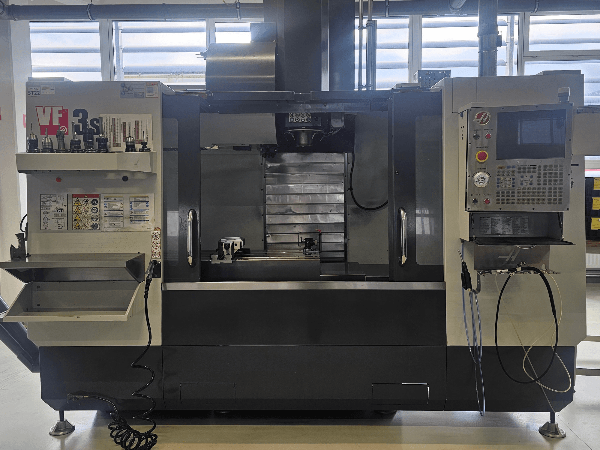 Haas VF3SS CNC-veski, esivaade, kus on tööriistahoidjad, juhtpaneel ja tühi jahutusvedeliku salv, ohutusmärgised nähtavad.