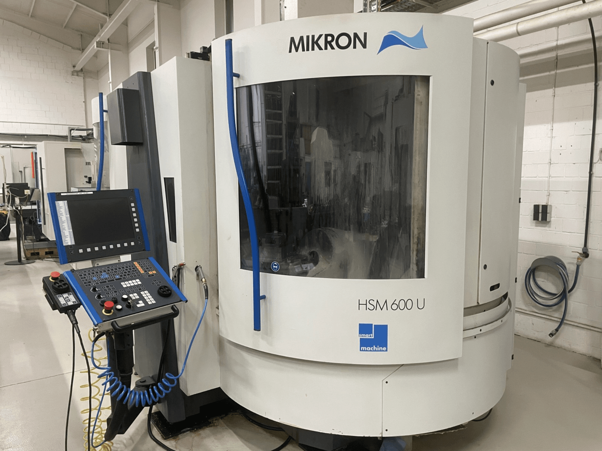 MIKRON HSM600U vertikaalne töötluskeskus esiplaanilt, millel on operatiivne juhtpaneel ja suur vaateaken.