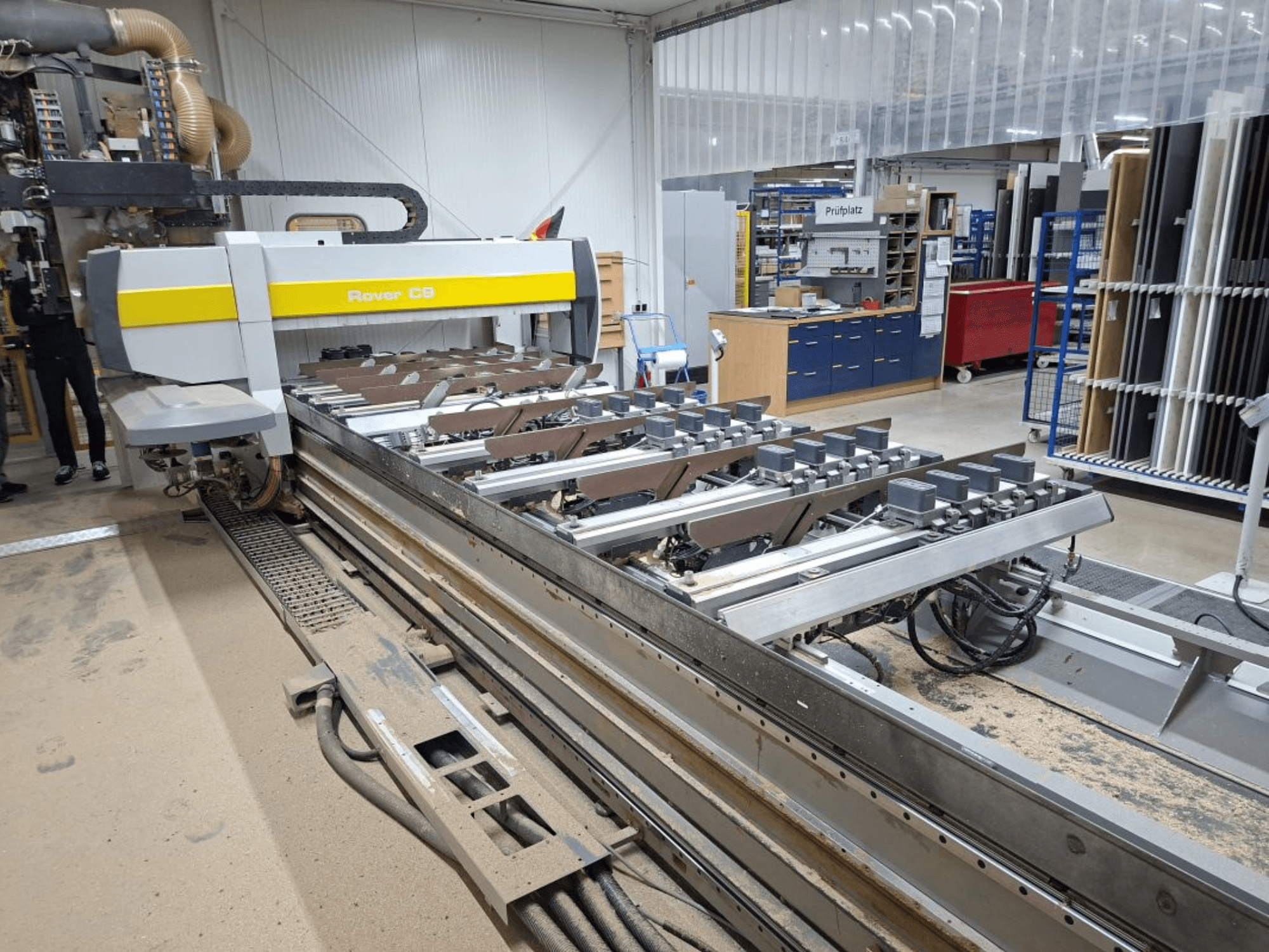 Rover C9 CNC-tööpink töökojas; esiplaanil on lõiketööriistad ja konveierisüsteem, põrandal on tolmu kogunemine.