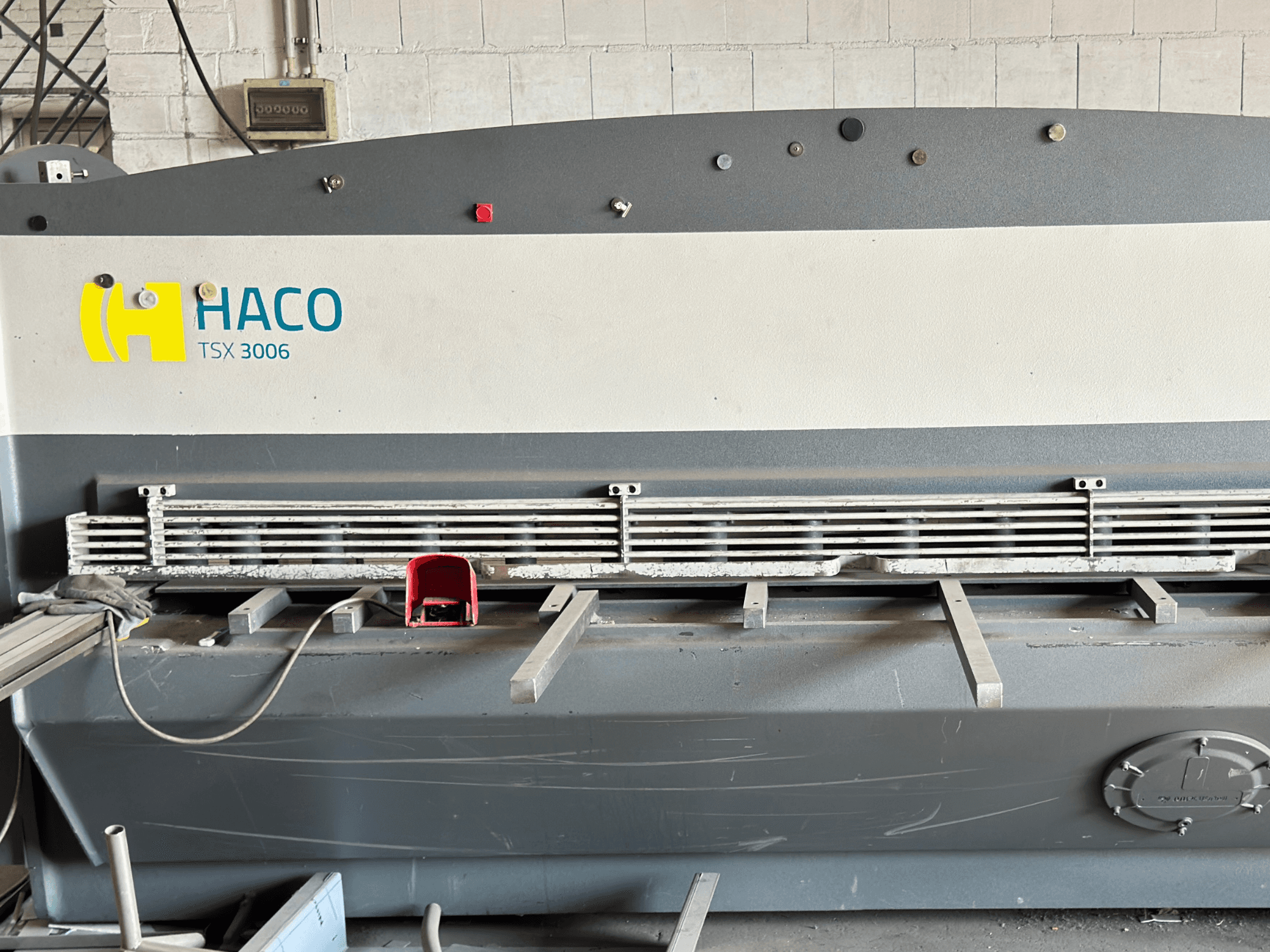 HACO TSX3006 MOT hüdrauliline lõikemasin, esiplaanil, metallist lõiketerade ja juhtpaneeliga, millel on näidatud töötamise üksikasjad.