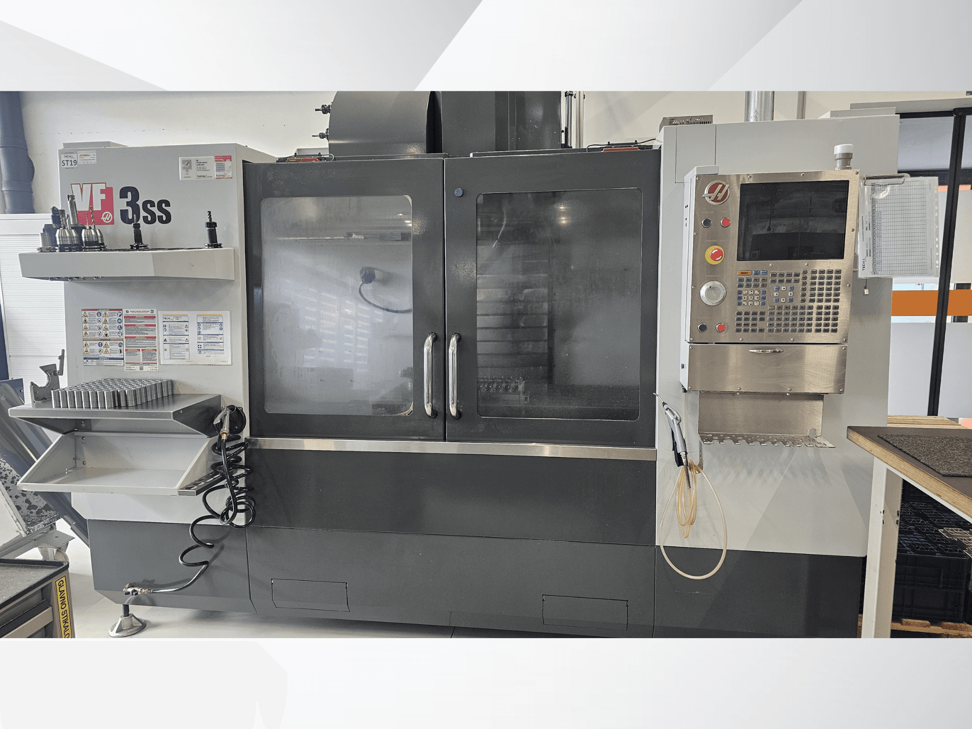 HAAS VF-3SS vertikaalne töötluskeskus, esiplaanil, juhtpaneel, tööriistahoidik ja suur klaasuks.