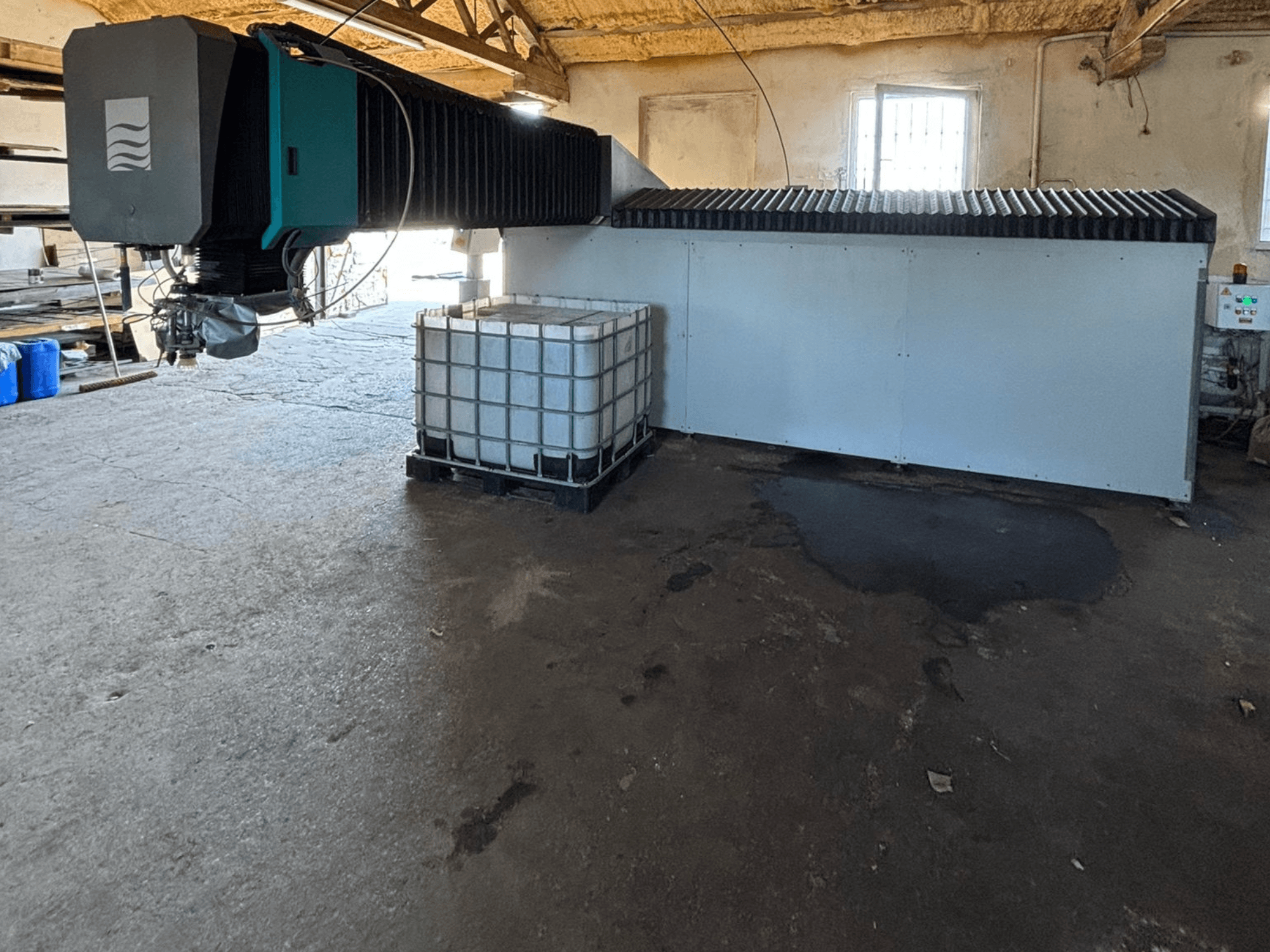 Tööstuslik veepihustusseade töökojas, külgvaade, kõrval on näha suur veepaak ja juhtpaneel.