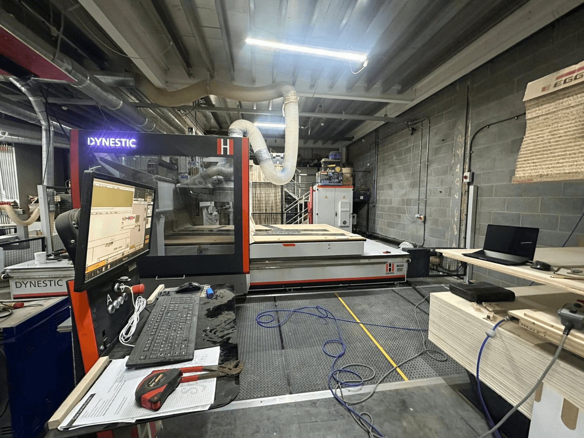 HOLZHER Dynestic 7535 puiduveski töökojas, näidatakse juhtpaneeli, monitori ja materjale töölaual, esiplaanil.