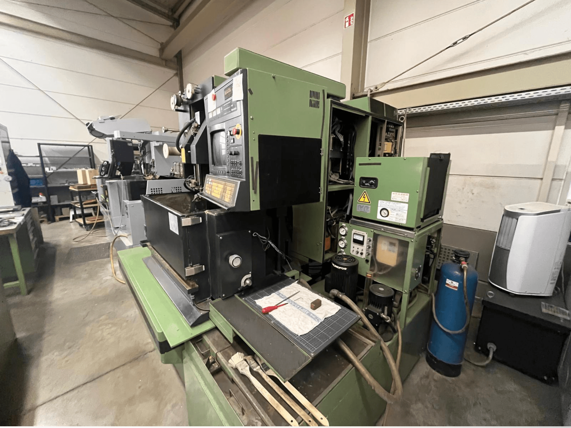 Roheline tööstuslik masin koos juhtpaneeliga, külgvaade; sisaldab hüdraulikakomponente ja tööpinda koos tööriistadega.