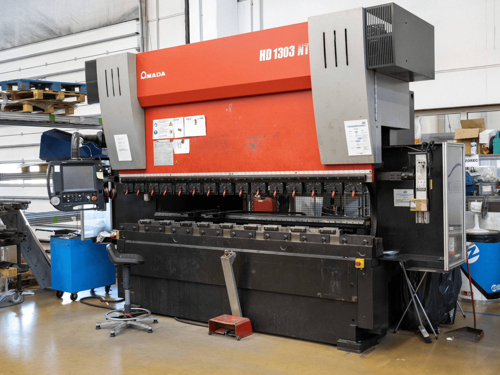 Amada HD 1303 hüdrauliline presspink töökojas, esivaade; mitu klambrit, juhtpaneel ja reguleeritav stool.