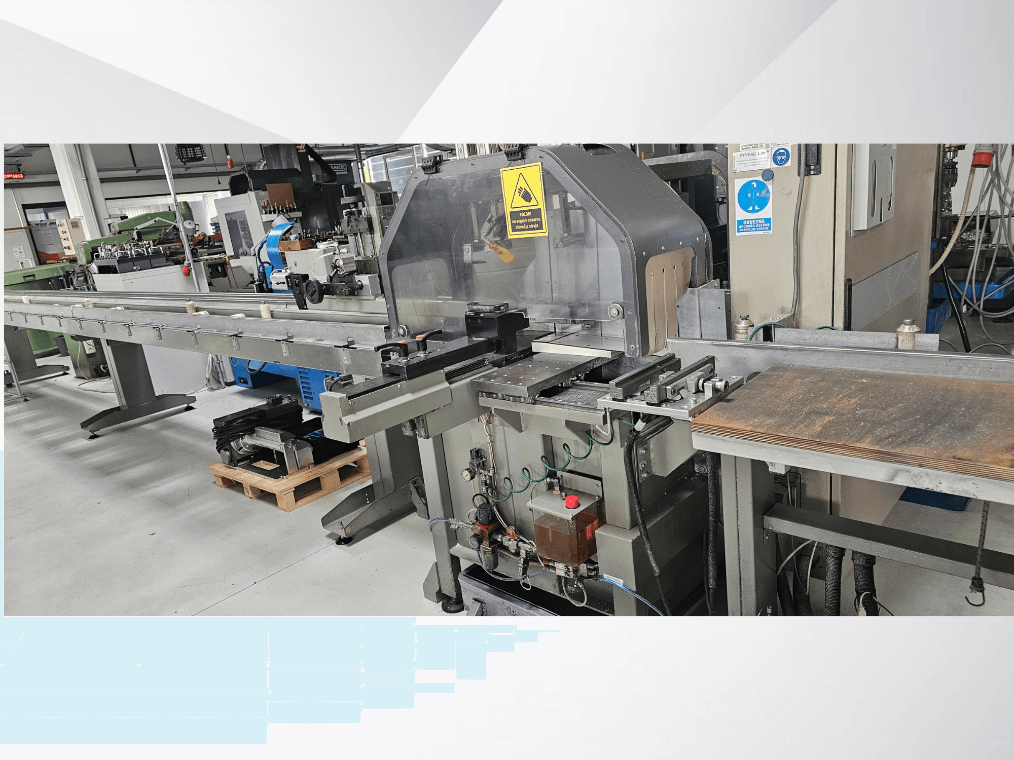 Tööstuslik lõikemasin külgvaates, millel on pikk konveier, juhtpaneel ja ohutushoiatused.