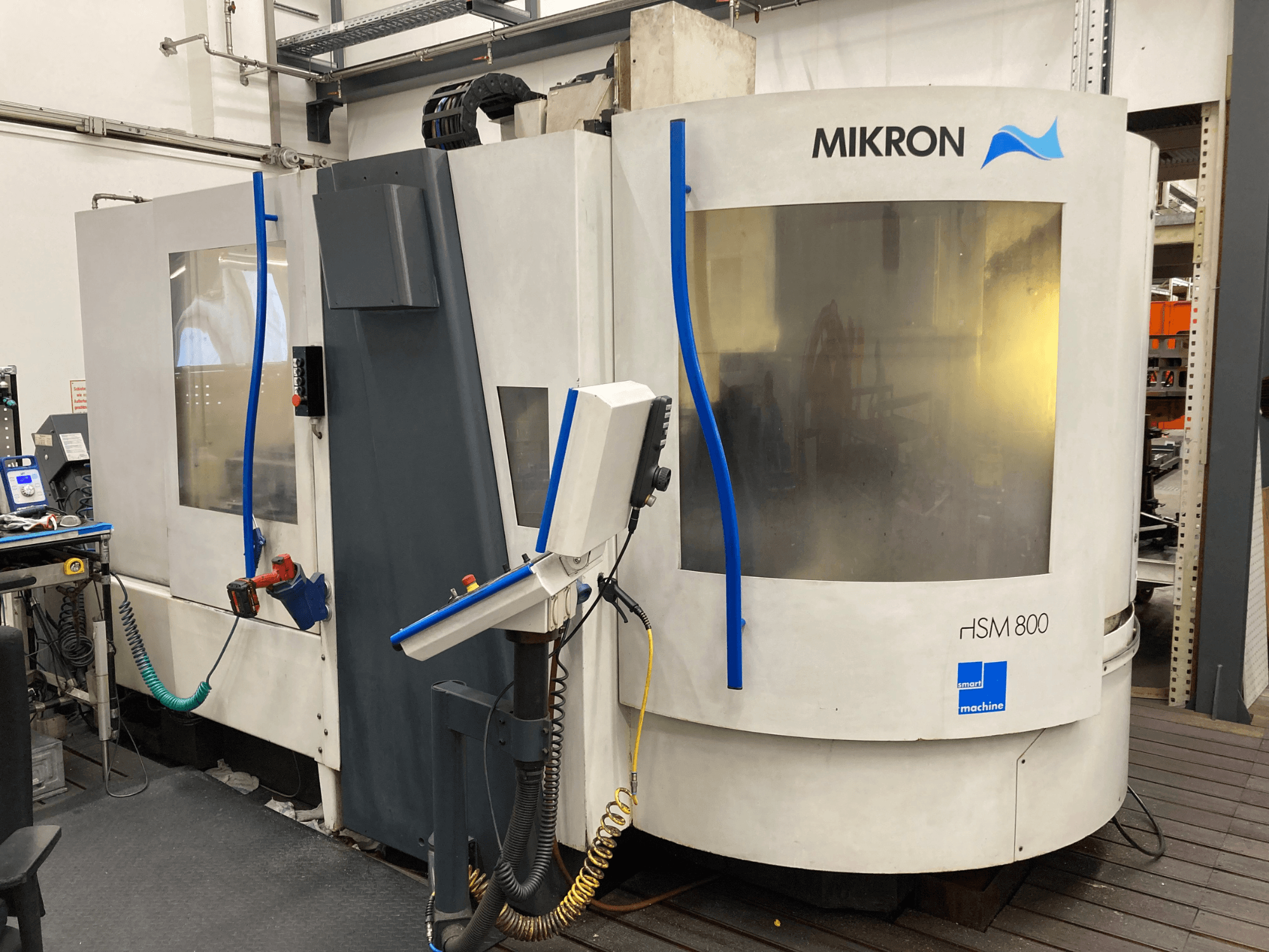 Mikron HSM 800, CNC-töötluskeskuse külgvaade koos juhtpaneeli ja tööriistahoidjaga, nähtavad voolikud ja kaablid.