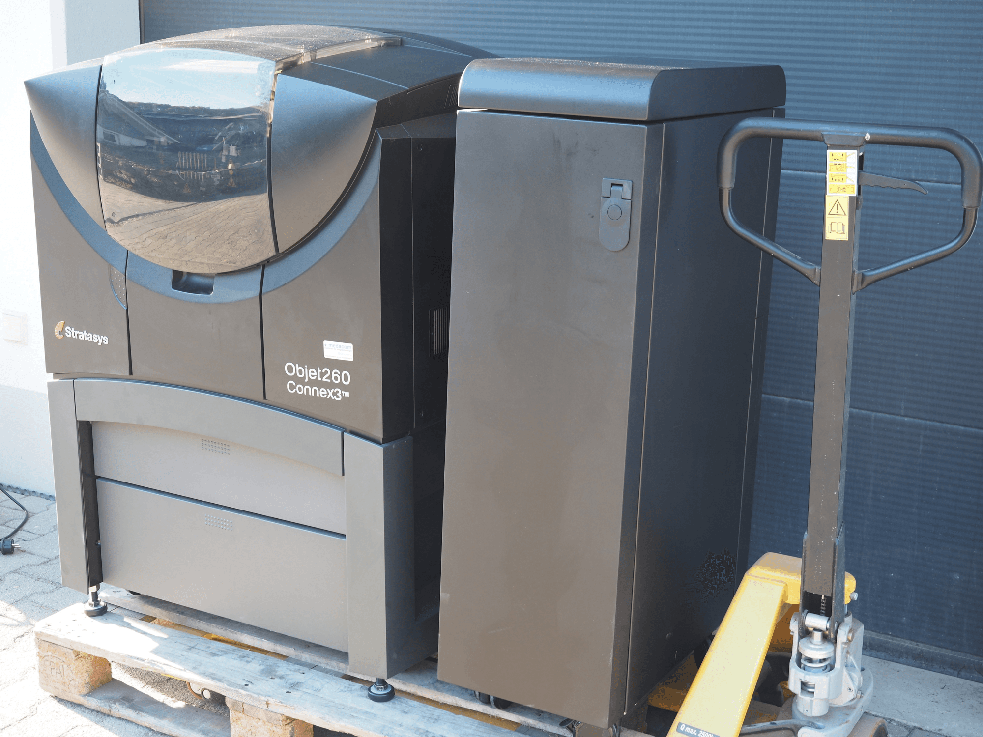 Stratasys Objet260 Connex3 plastikust 3D-printer, külgvaade, kompaktse konstruktsiooniga juhtpaneel ja ühendatud materjalikast.