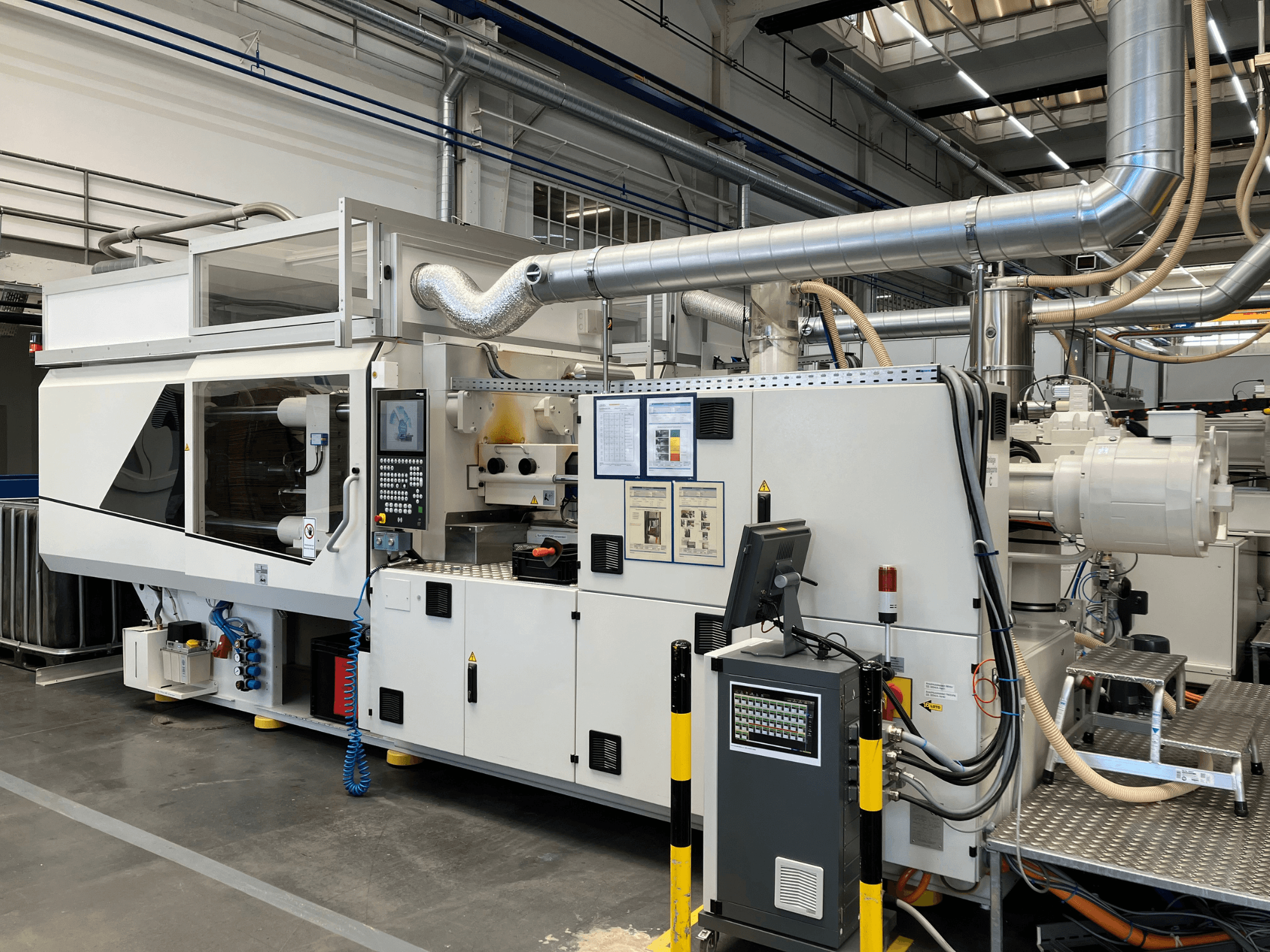 Tööstusmasina esivaade koos juhtpaneeli, torude ja ekraanidega, millel on elegantne valge disain ja tehnilised detailid.