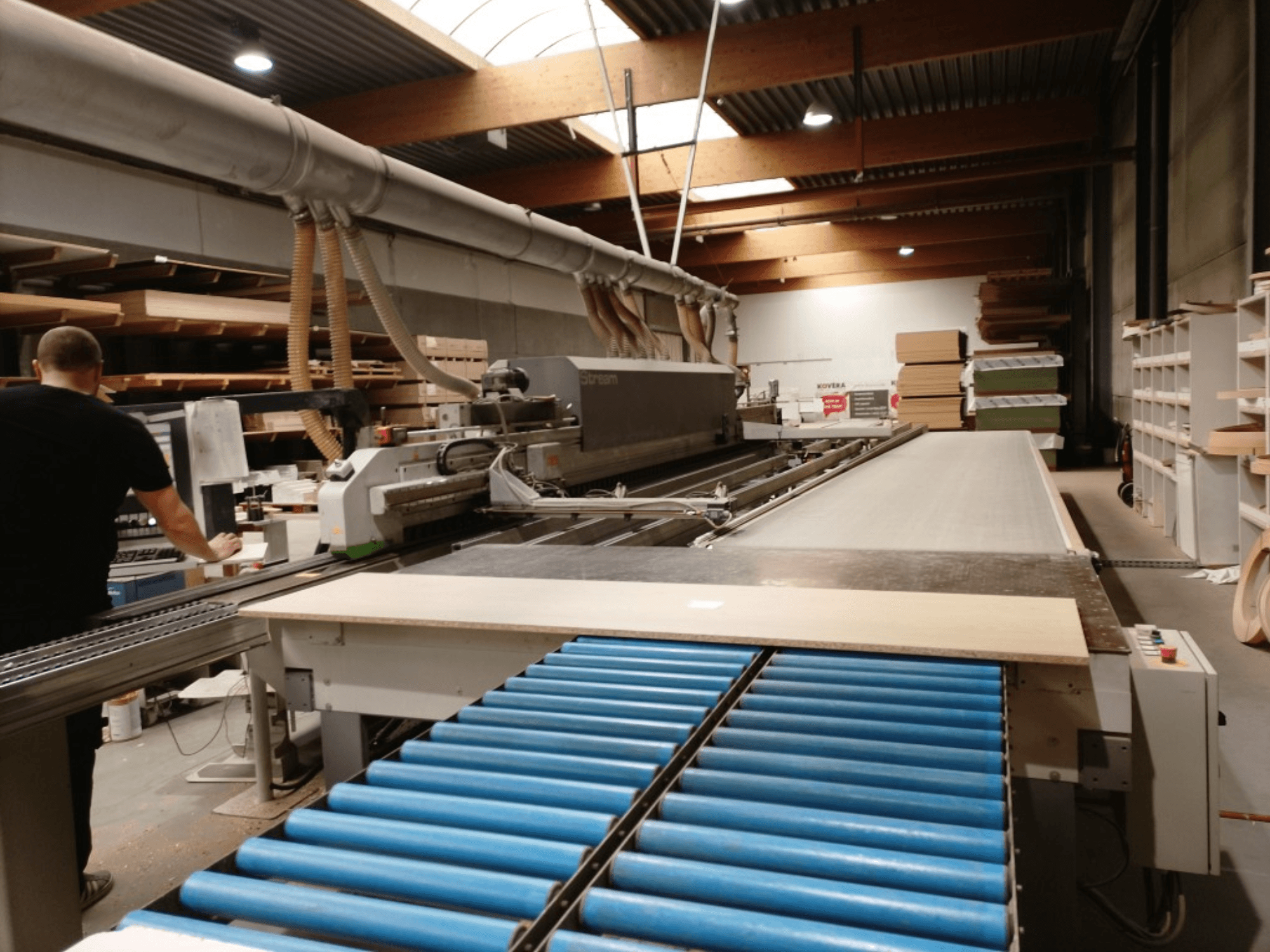 BIESSE Edge Stream B1 servakandur, külgvaates on näha operaator, sinised rullid ja puitplaat konveieril.