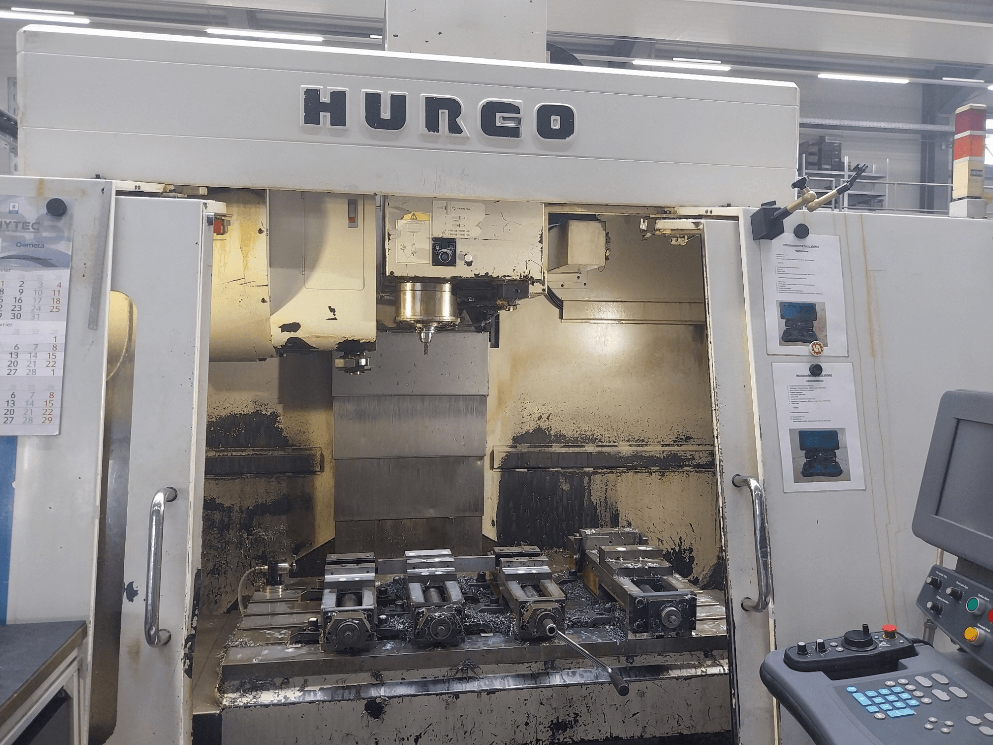 Hurco VMX 42 vertikaalne töötluskeskus esivaates, millel on töölaud koos kinnituste ja juhtpaneeliga, veidi kulunud seisukorras.