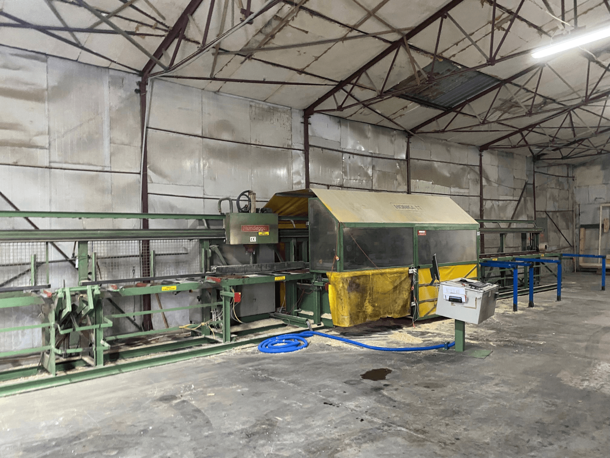 CNC-puidutöötluskeskus HUNDEGGER K1 töökojas, külgvaates on näha masinad, juhtimisseadmed ja saepuru põrandal.