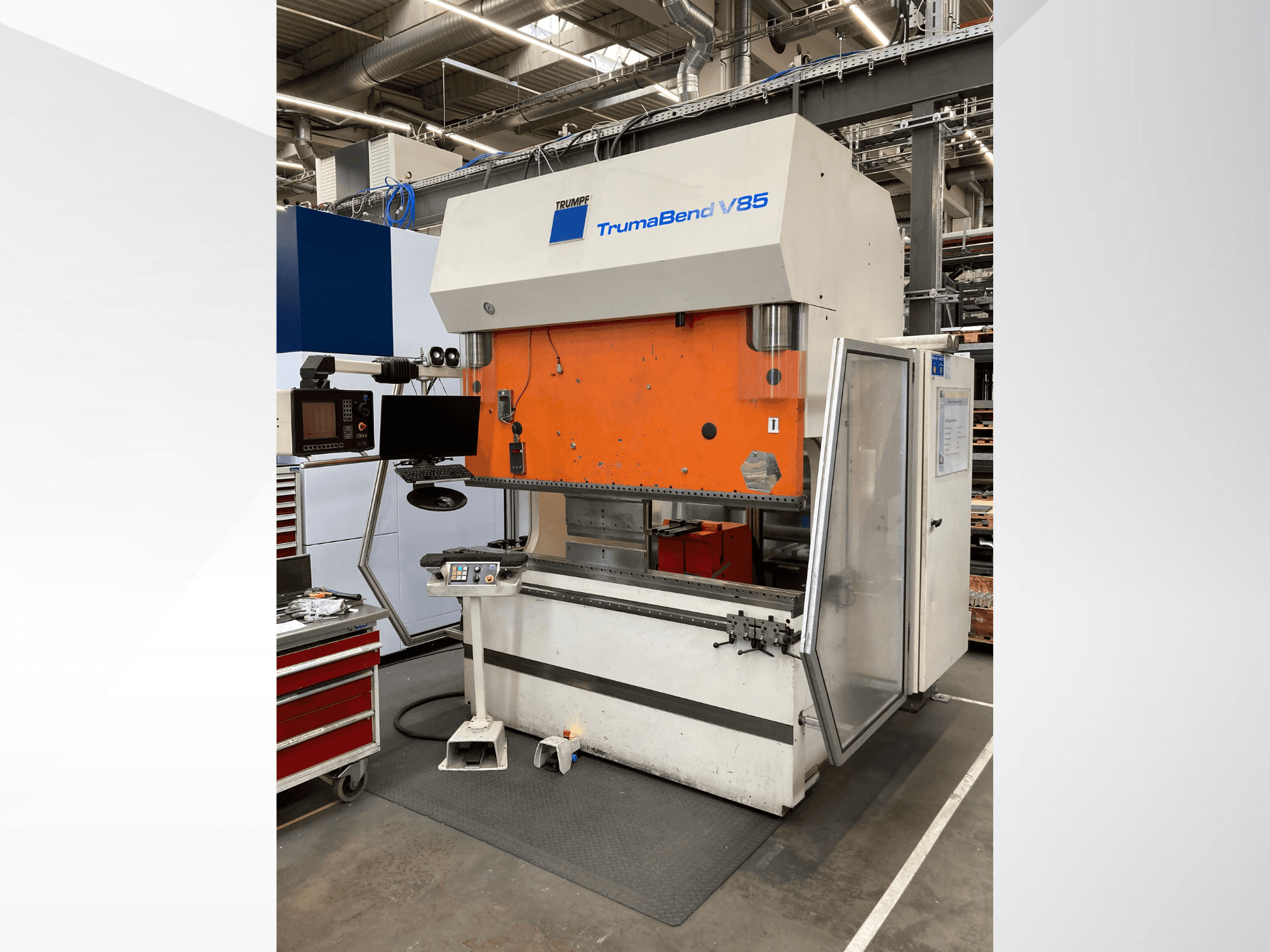 TruMatic V85 painutusmasin tehases, millel on oranž esipaneel, juhtimisekraan ja avatud küljeuks, külgvaade.