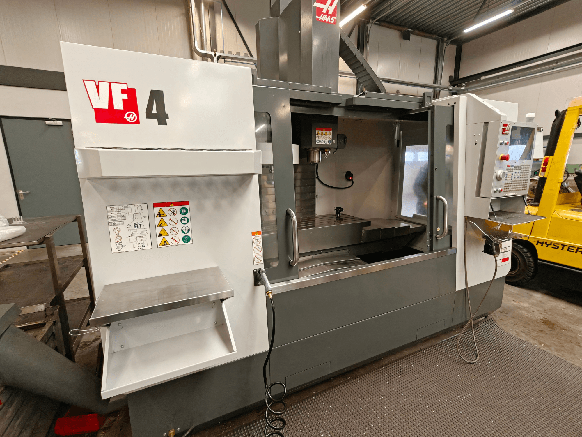 HAAS VF-4 vertikaalne töötluskeskus, esiplaan, juhtpaneel, tööala ja küljel olevad ohutussildid.