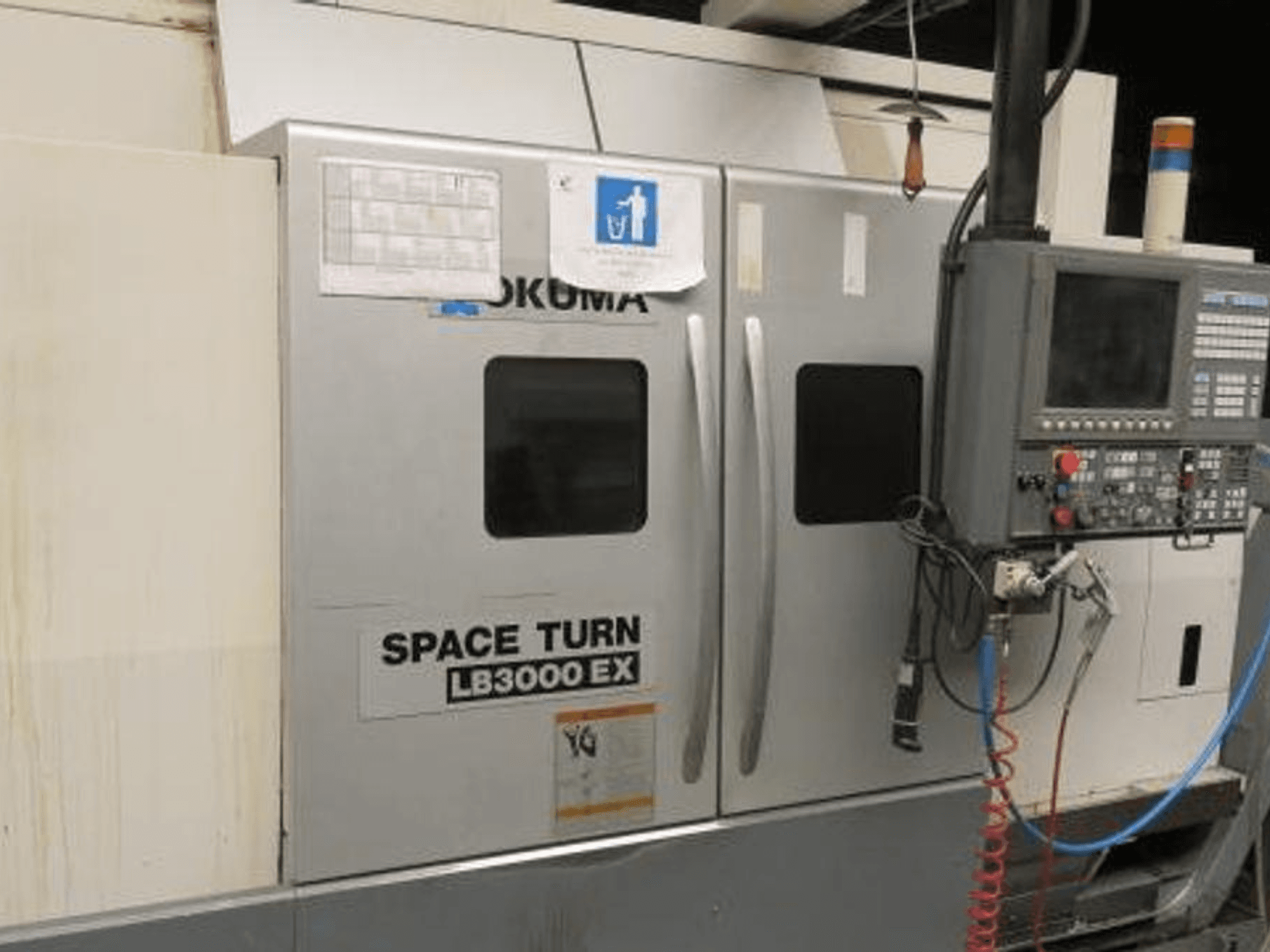 Okuma Space Turn LB3000 EX CNC-tööpink, külgvaade, millel on juhtpaneel, kaks ust ja nähtavad juhtmed.