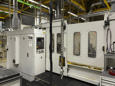 Tööstuslik CNC-masin koos juhtpaneeliga, külgvaade; aknad, ketid ja metallkomponendid tehases.