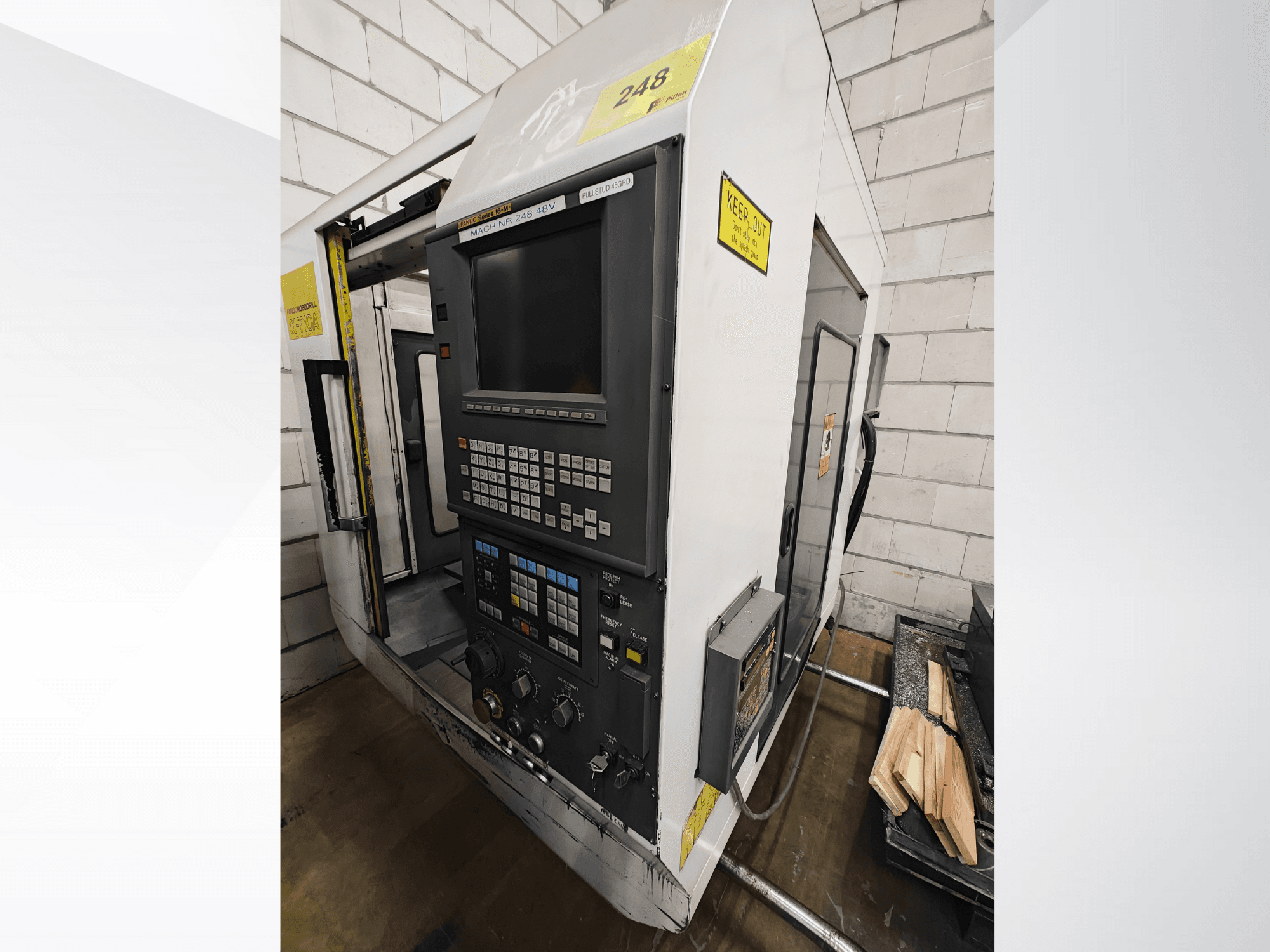 CNC-tööpink nr 248, esiplaan, millel on juhtpaneel koos nuppude ja ekraaniga, kõrval riiulil puidutükid.